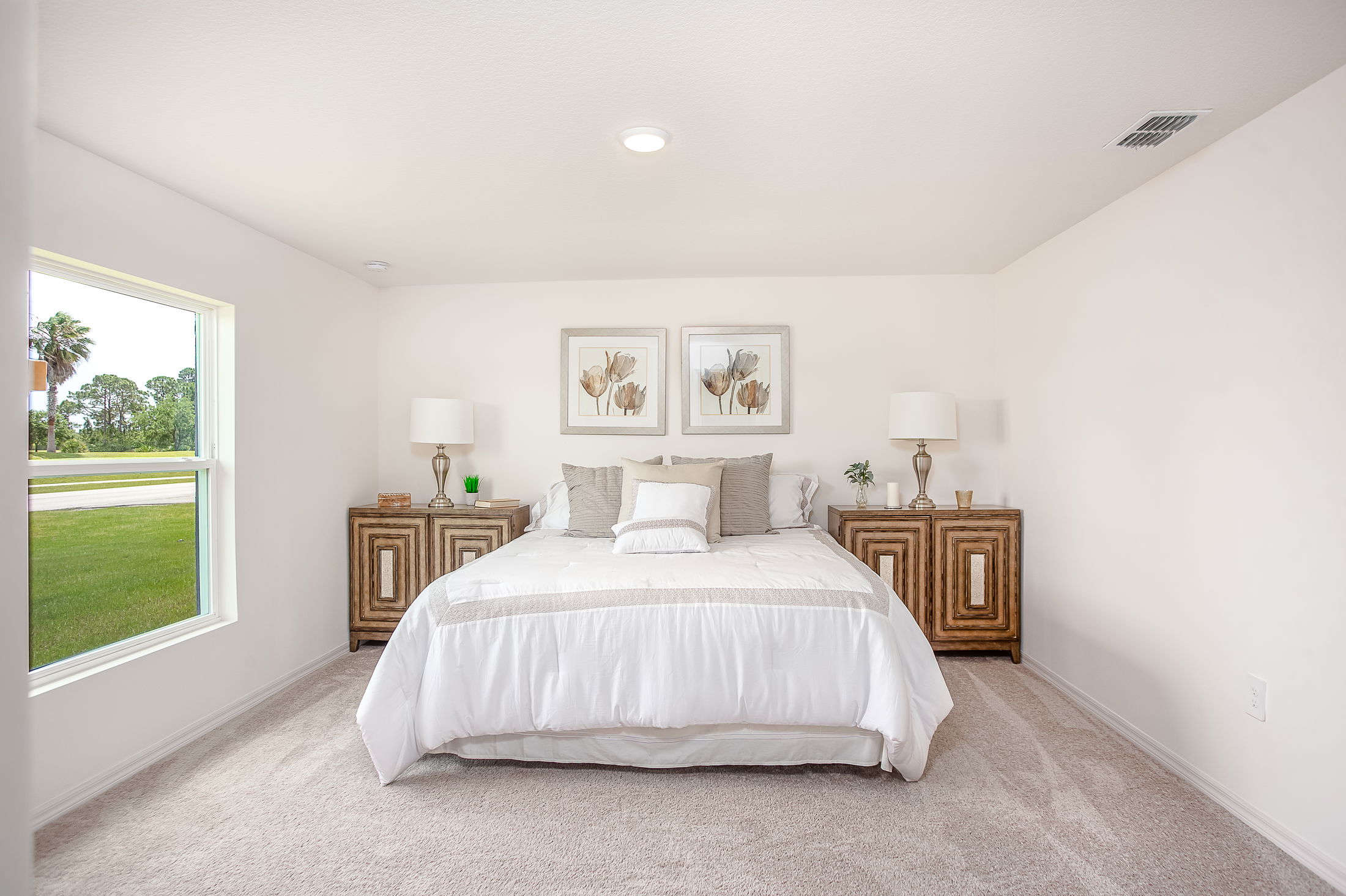 Modern bedroom with a large bed, white bedding, wooden side tables, and decorative wall art, featuring natural light from a window.
