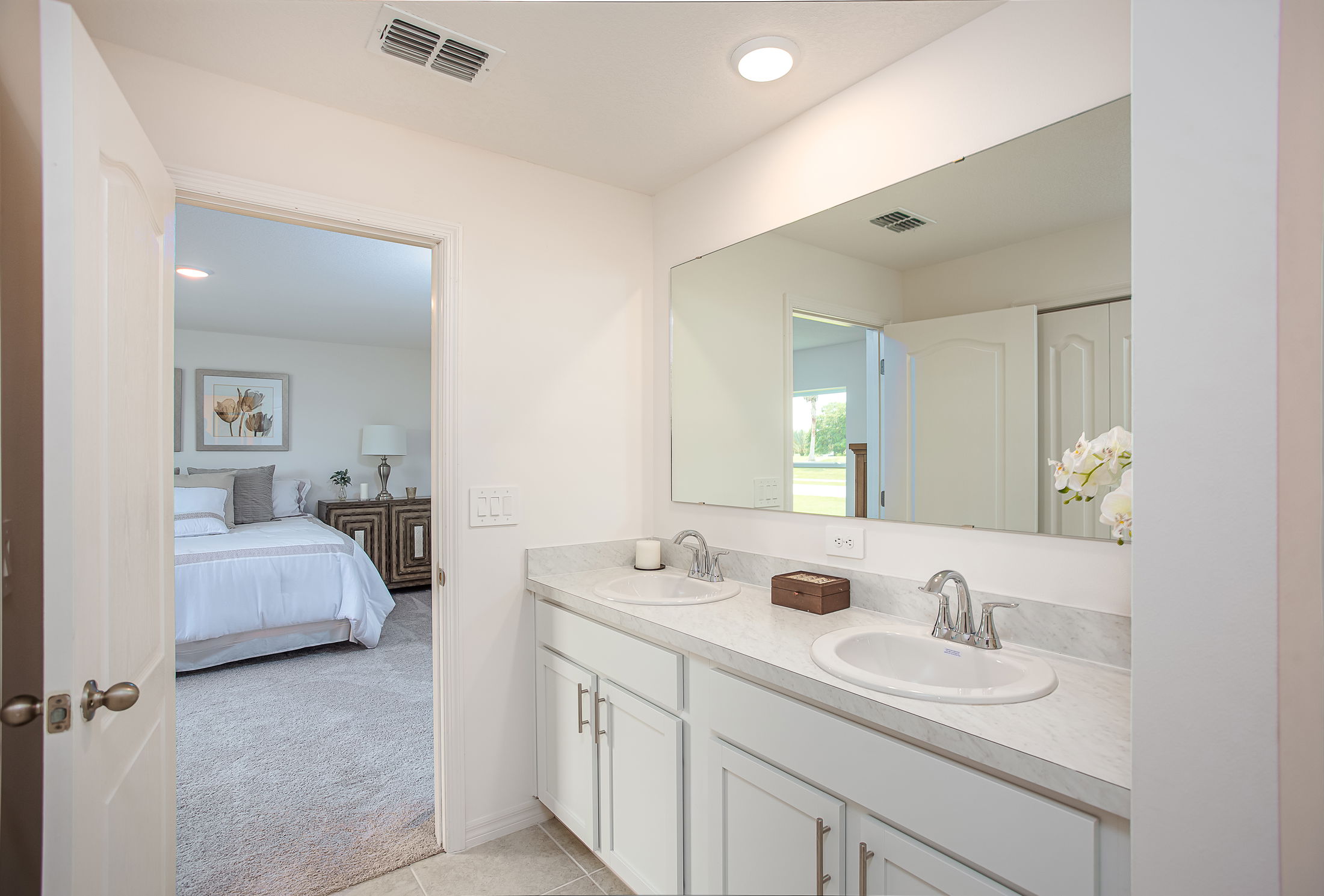 Modern bathroom with a double sink vanity and view into a cozy, well-decorated bedroom.