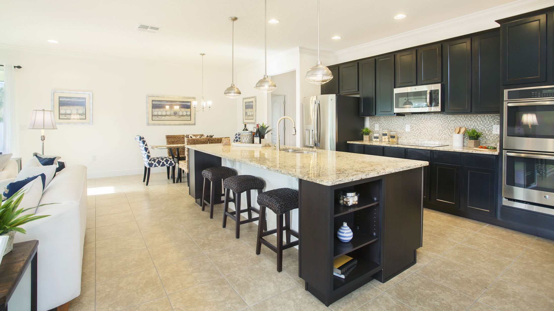 Modern kitchen interior with a large granite island, dark cabinetry, stainless steel appliances, and pendant lighting.