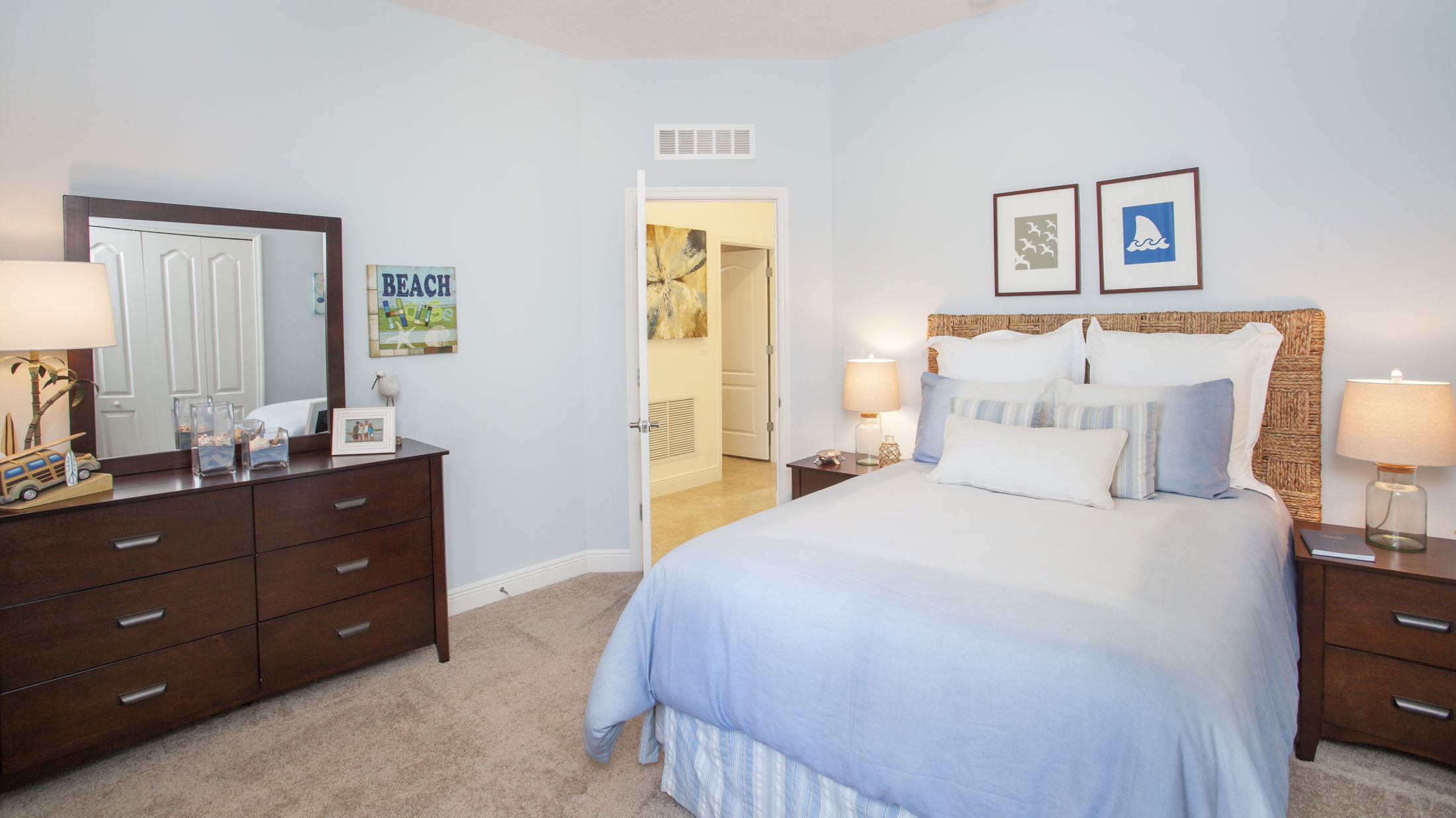 Cozy bedroom with light blue walls, a wicker headboard, and wooden furniture, featuring beach-themed decor and soft lighting.