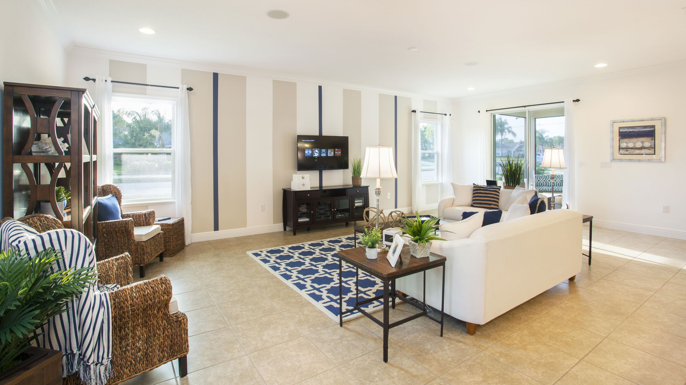 Spacious modern living room with white sofas, rattan chairs, blue accents, and large windows providing natural light.