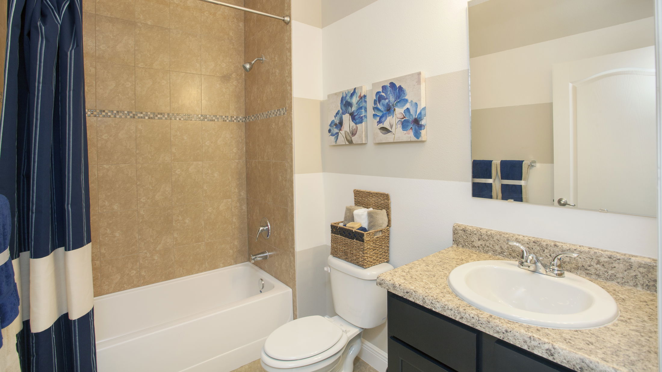 Modern bathroom with granite countertop, white sink, brown tiled shower, and blue floral wall art.