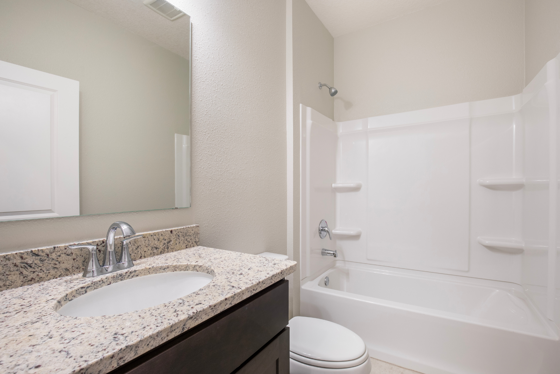 Modern bathroom featuring a granite countertop, large mirror, and a white bathtub with showerhead.