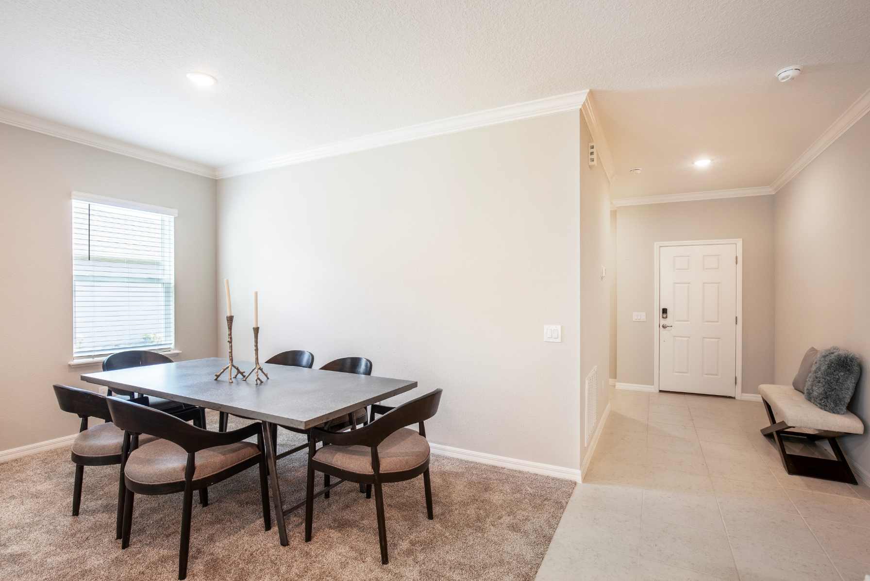 Modern dining area with a sleek table and chairs beside a neutral-toned entryway.