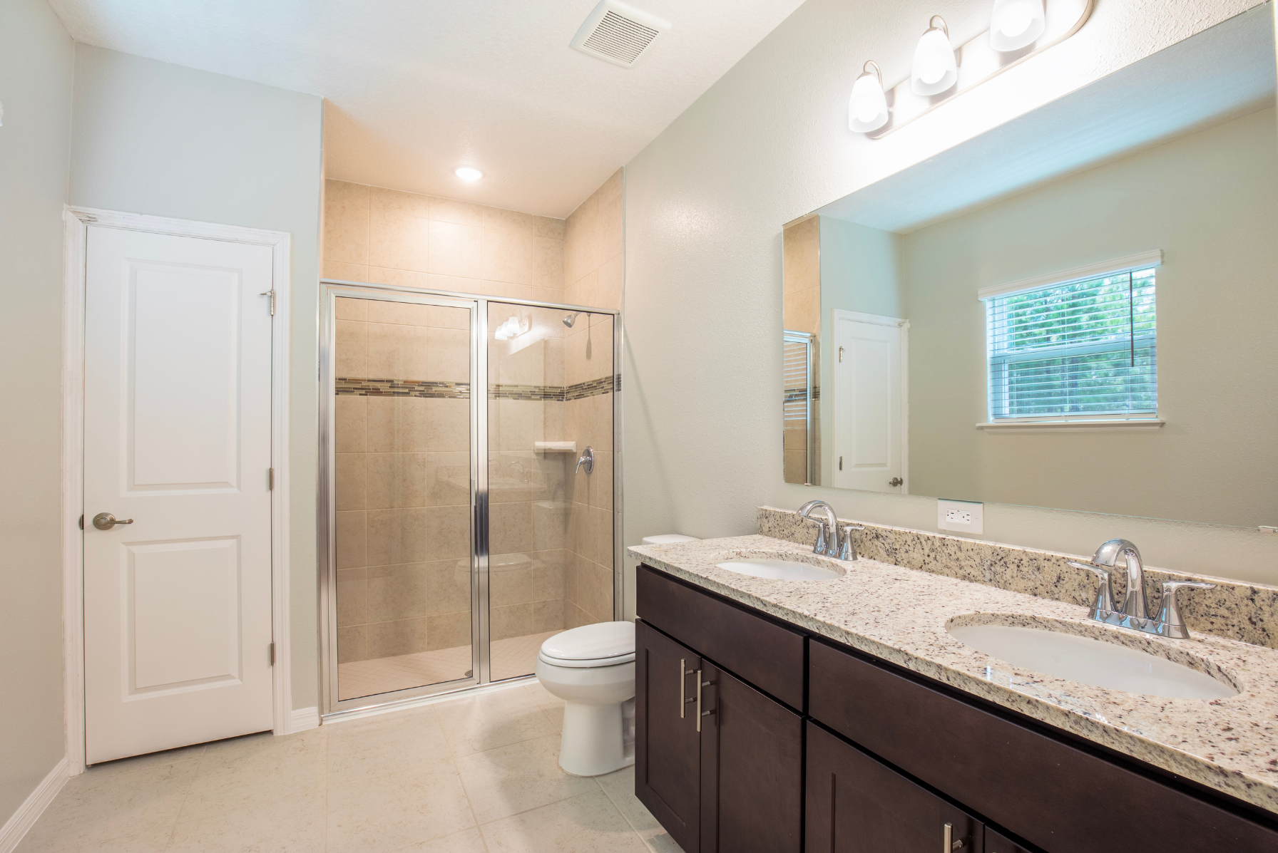 Modern bathroom with double vanity, granite countertops, and a glass-enclosed shower.