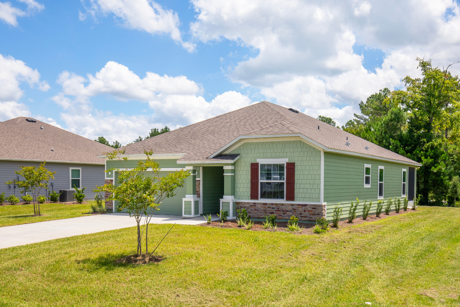 A modern green suburban home with a gable roof and landscaped yard under a clear blue sky.