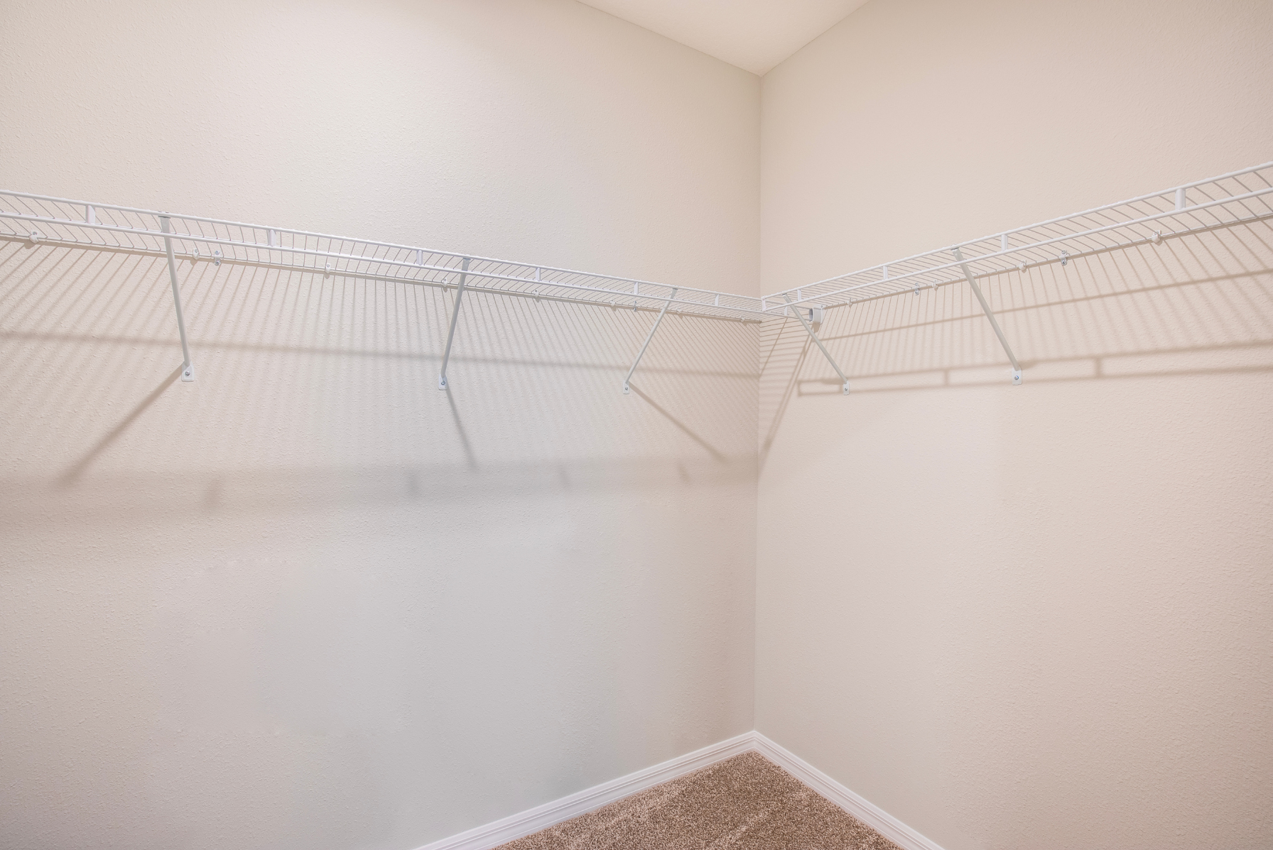 Spacious empty walk-in closet with wire shelving and beige walls.