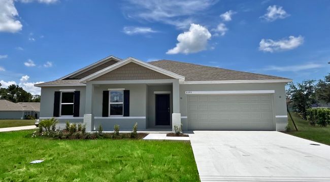 Modern single-story home with a two-car garage and well-maintained lawn under a clear blue sky.