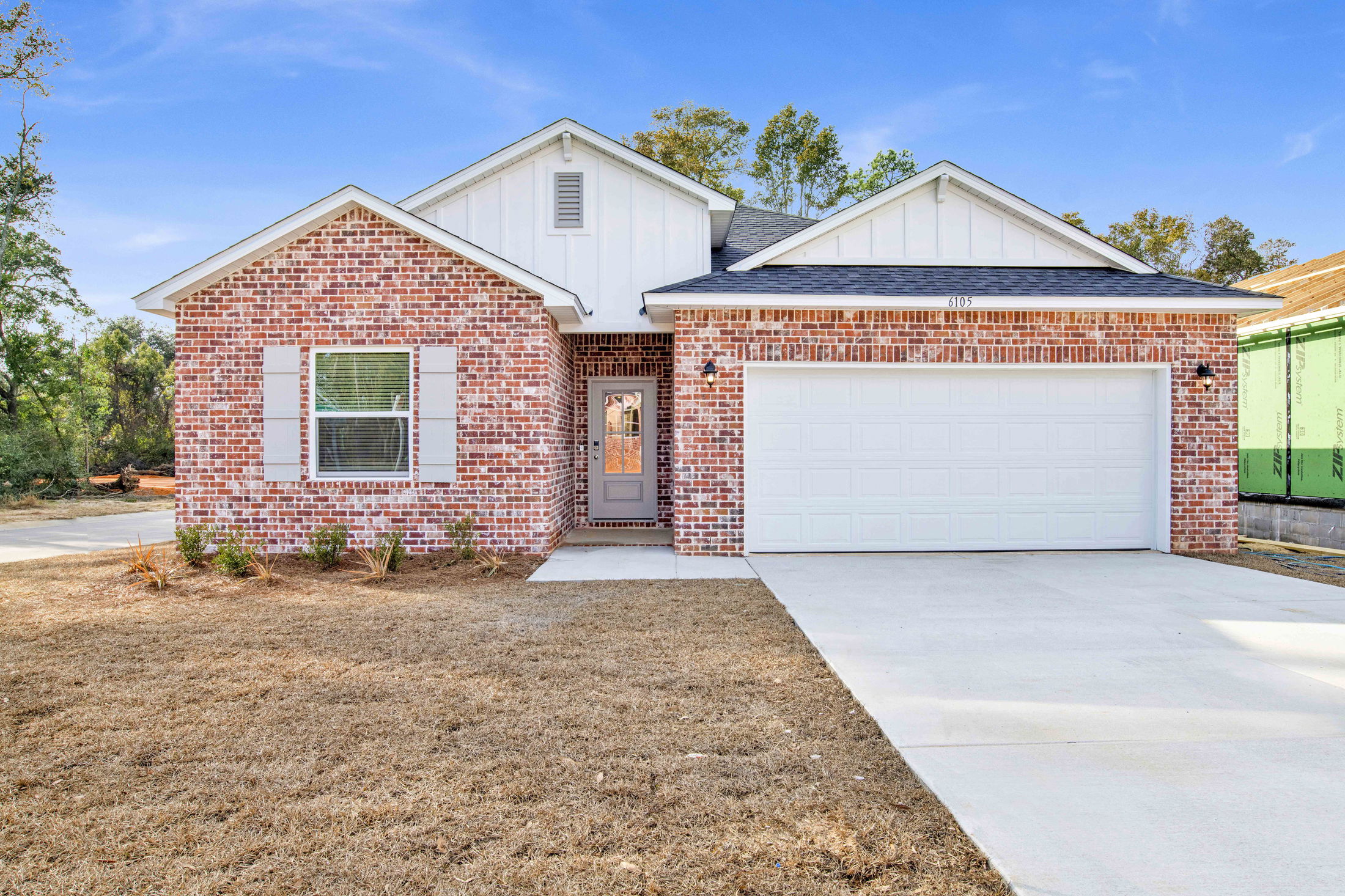 Newly built brick house with a spacious yard and two-car garage under a clear blue sky.