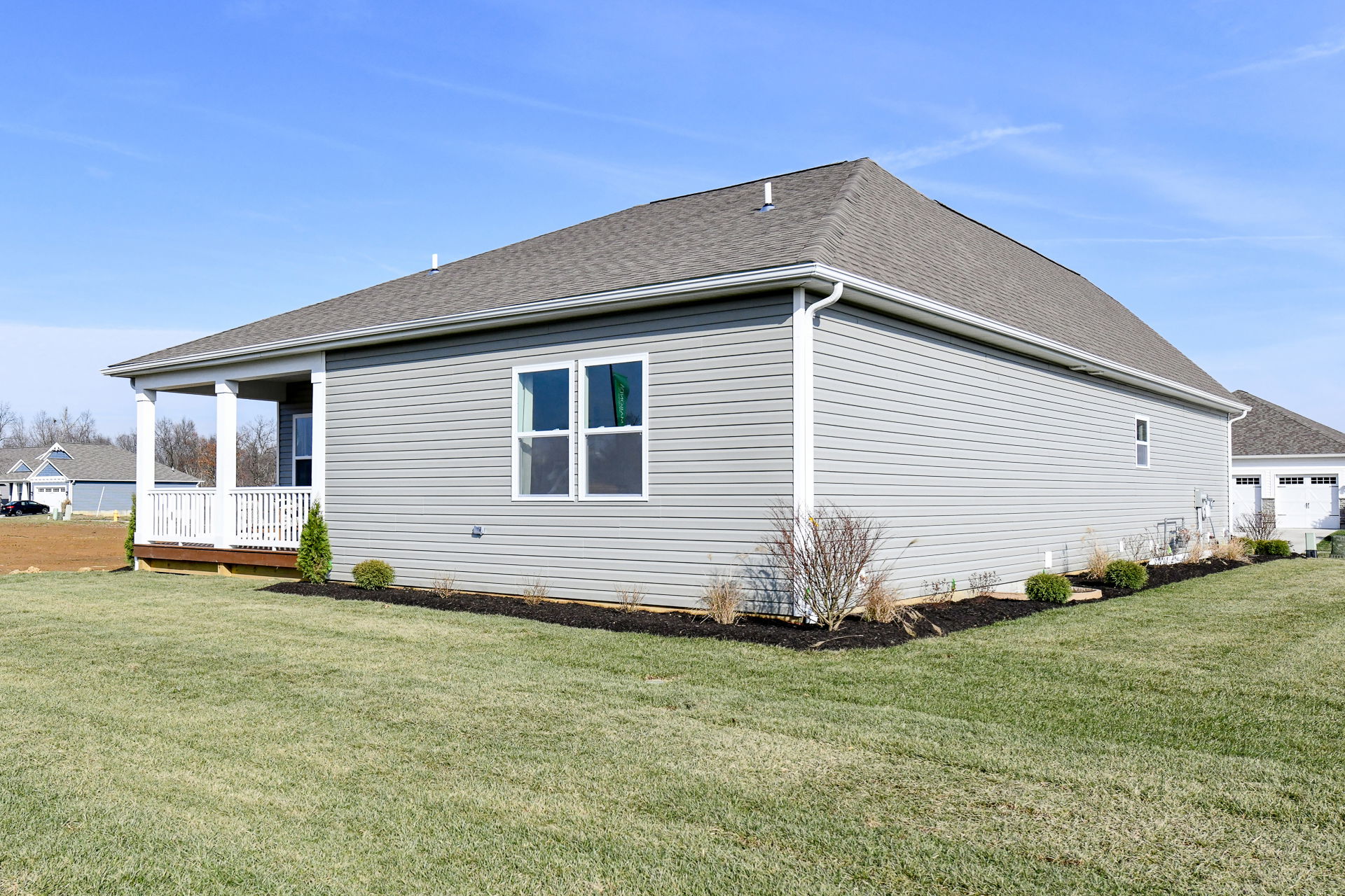 Modern single-story gray house with a manicured lawn and backyard porch on a sunny day.