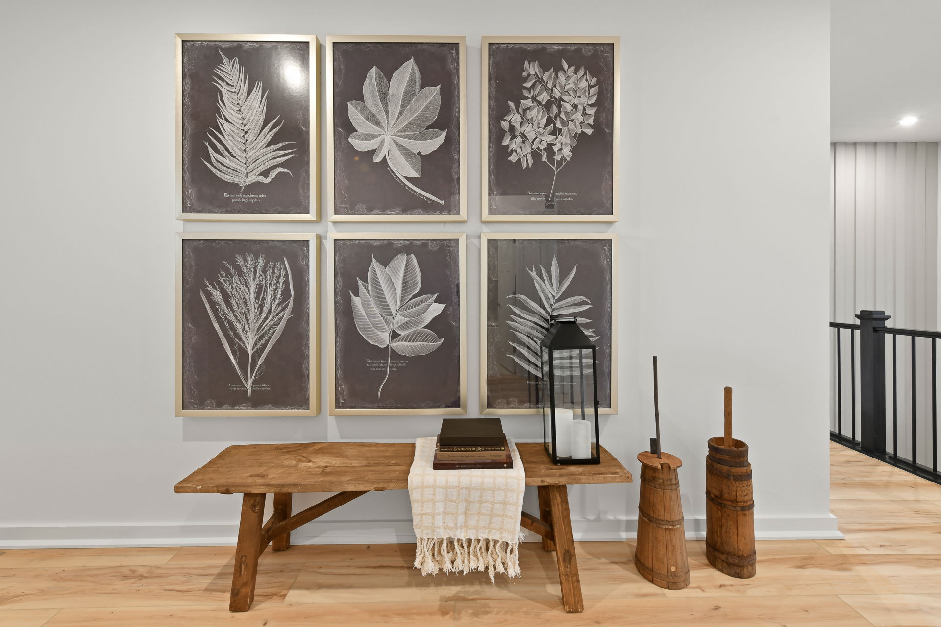 Stylish wall featuring six framed botanical leaf prints above a rustic wooden bench with decorative items in a modern interior setting.