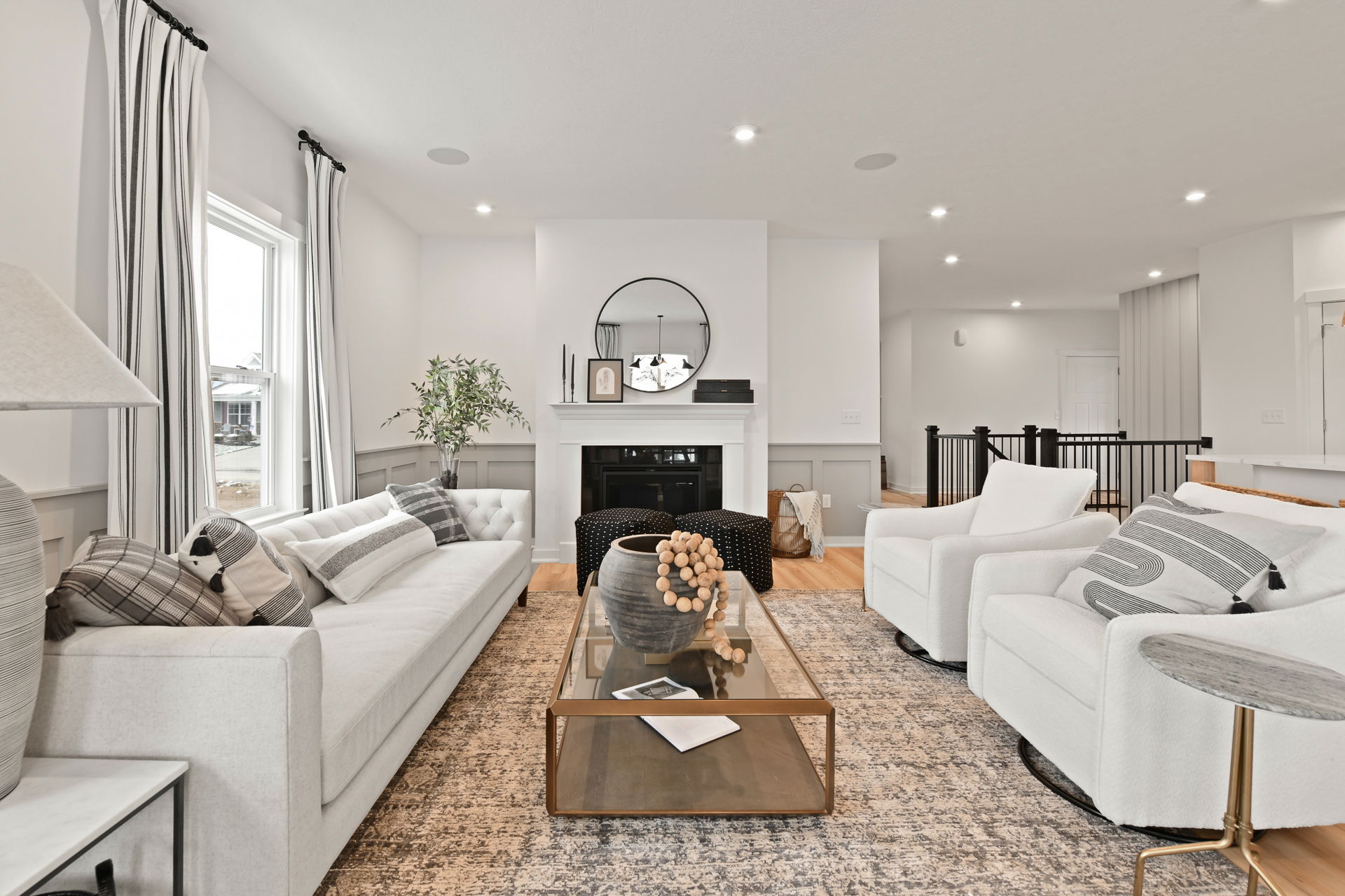 Modern living room with a sleek white sectional sofa, glass coffee table, and stylish decor, featuring a fireplace and black framed mirror.