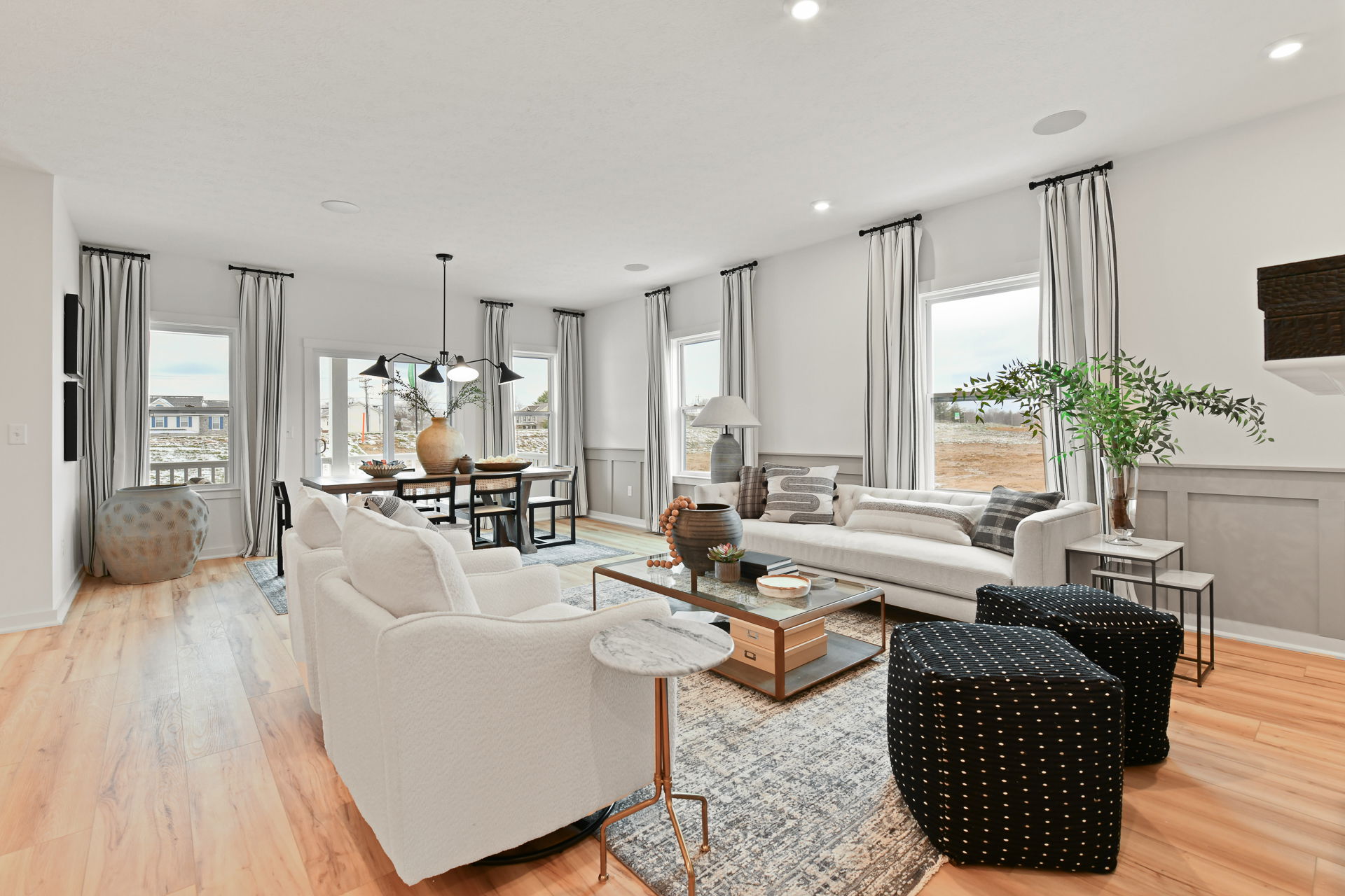 Modern living and dining room with light wood flooring, white furniture, striped curtains, and stylish decor.
