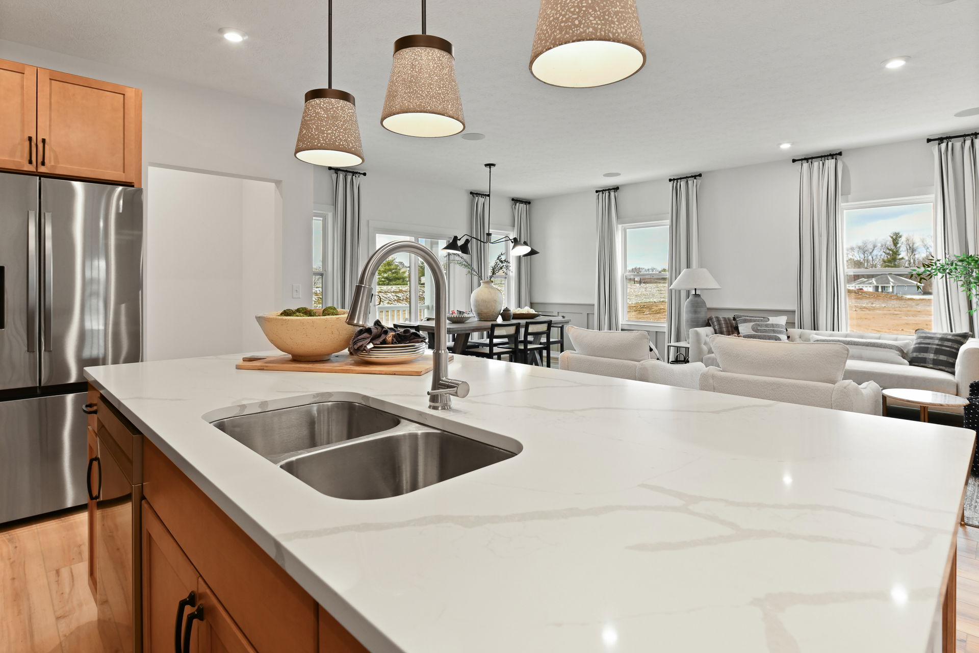 Modern open-concept kitchen and living room with a marble island countertop, stainless steel appliances, and elegant pendant lighting.