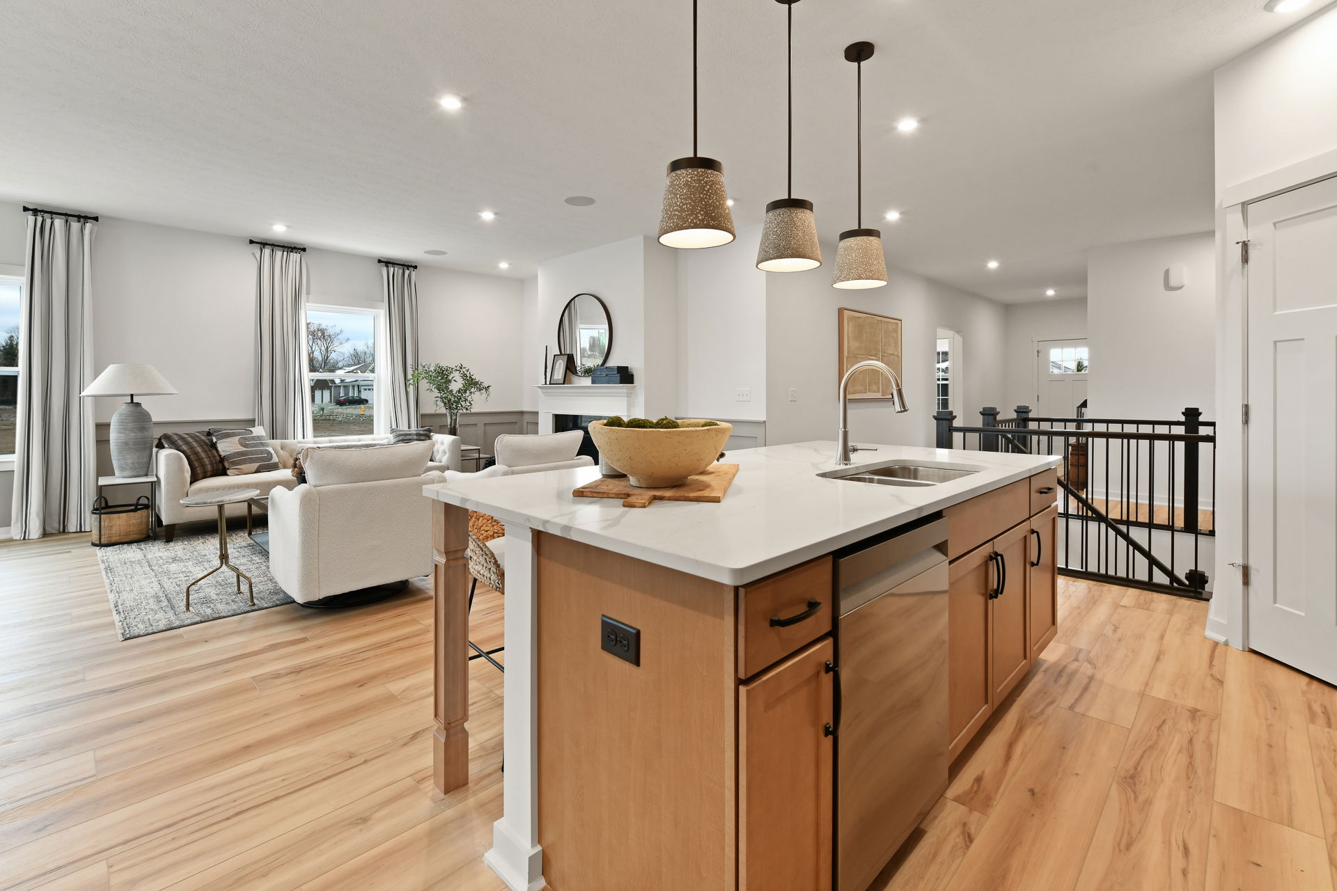 Modern open-concept living room and kitchen with wooden floors, white walls, and stylish lighting fixtures.