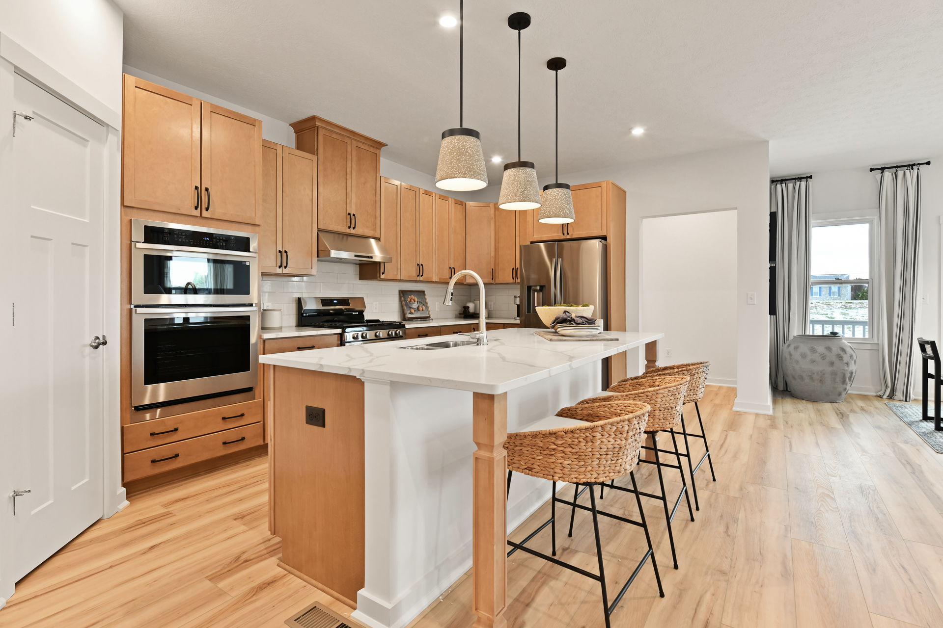Modern kitchen with wooden cabinets, stainless steel appliances, and a white marble island with wicker barstools.