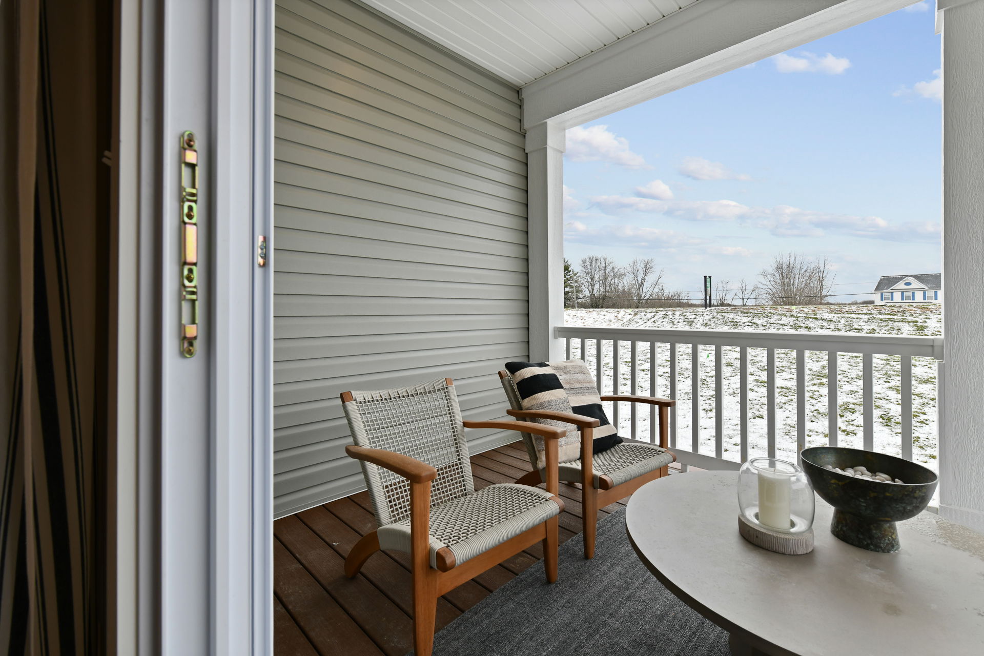 Cozy wooden patio chairs with cushions on a covered porch overlooking a snow-dusted landscape.