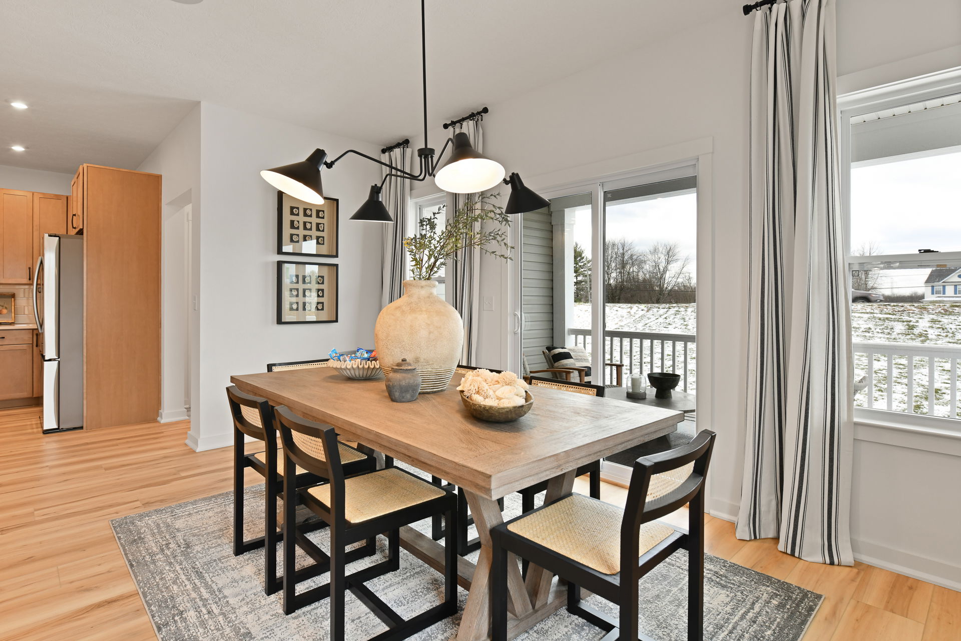 A modern dining room with a wooden table, black chairs, large vase centerpiece, and panoramic window view.