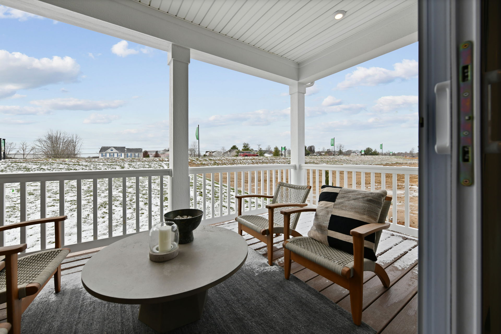 Cozy outdoor patio with wicker chairs, a table, and a view of a snowy landscape and distant houses.