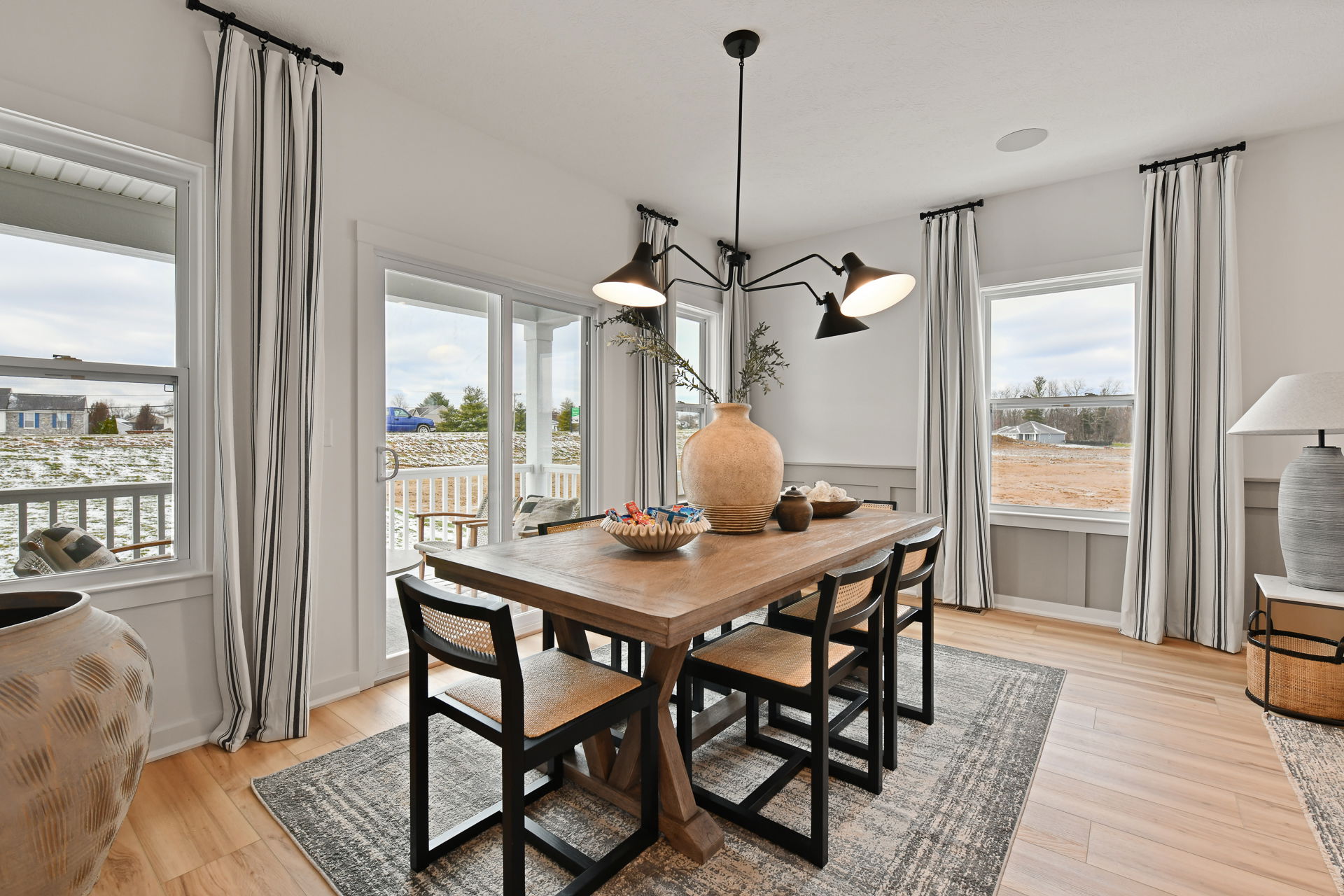 Stylish modern dining room with a wooden table, black chairs, large vases, and natural light from surrounding windows.