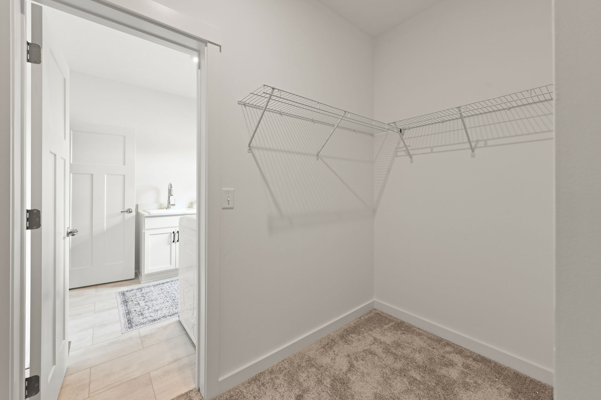 A spacious walk-in closet with carpet flooring and wire shelving, adjacent to a laundry room with modern appliances.