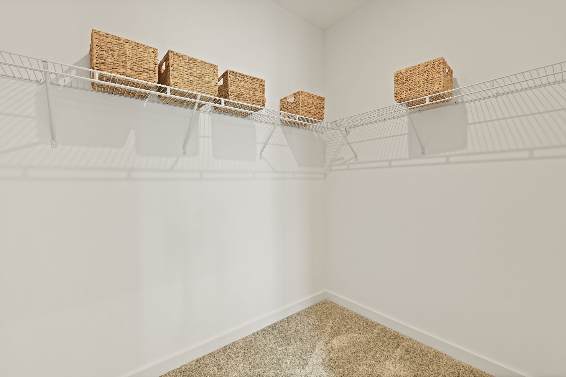 Empty walk-in closet with white walls and wire shelving holding wicker storage baskets.