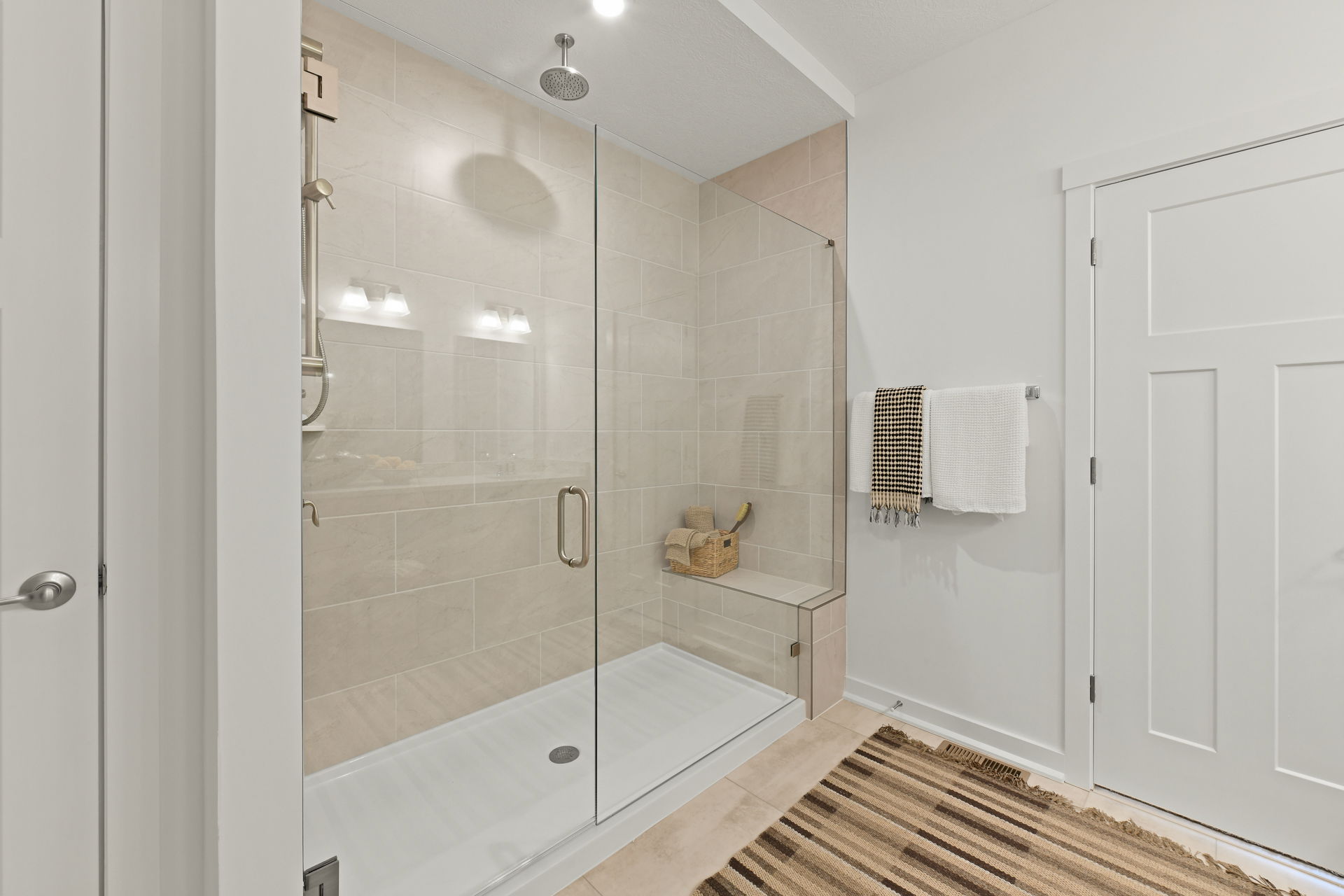 Modern bathroom featuring a glass-enclosed shower with beige tiles, dual shower heads, and a neatly organized towel rack.