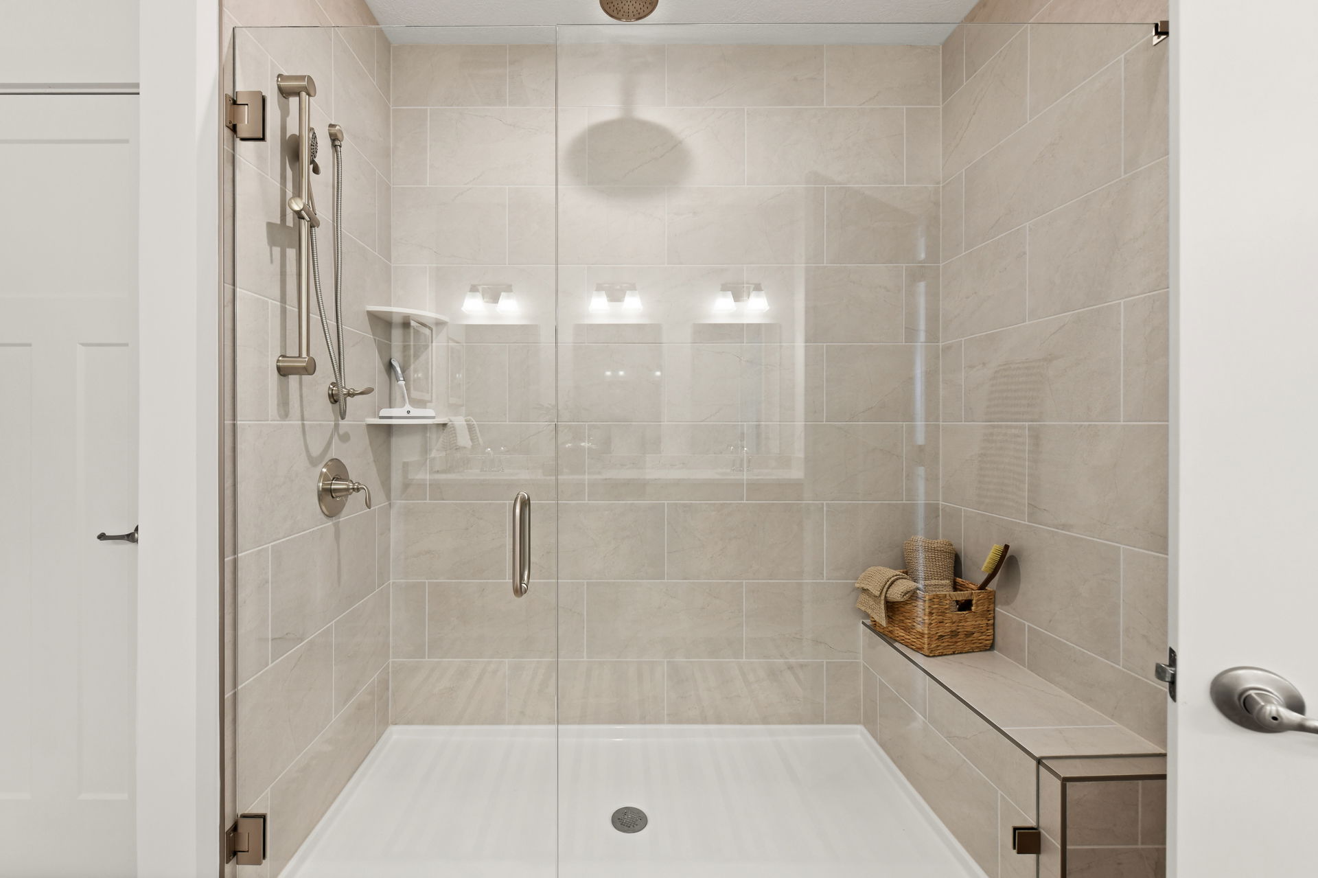 Modern bathroom shower area with beige tiles, glass doors, and wall-mounted shower fixtures.