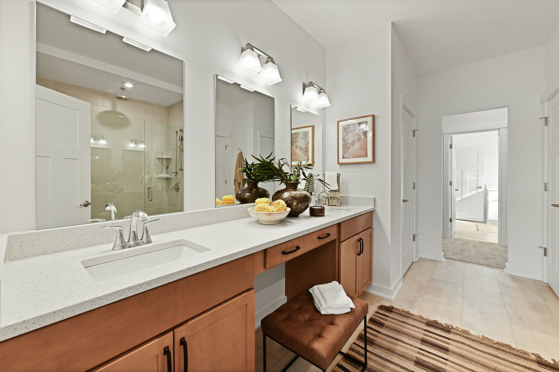 Modern bathroom vanity with double sinks, wooden cabinets, decorative plants, and a view into a shower area.