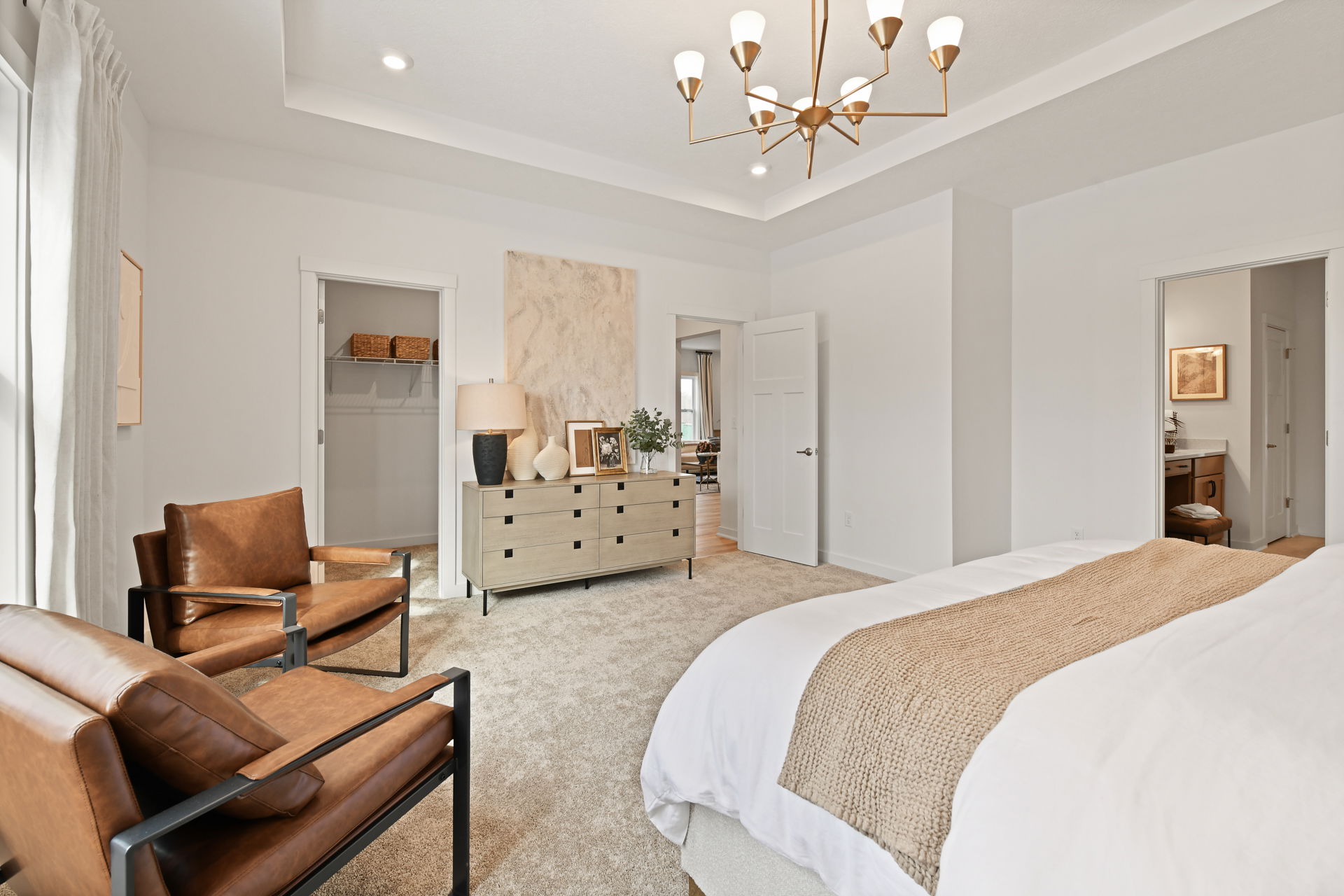Modern bedroom interior with a cozy beige carpet, stylish wooden dresser, leather armchairs, and elegant chandelier.