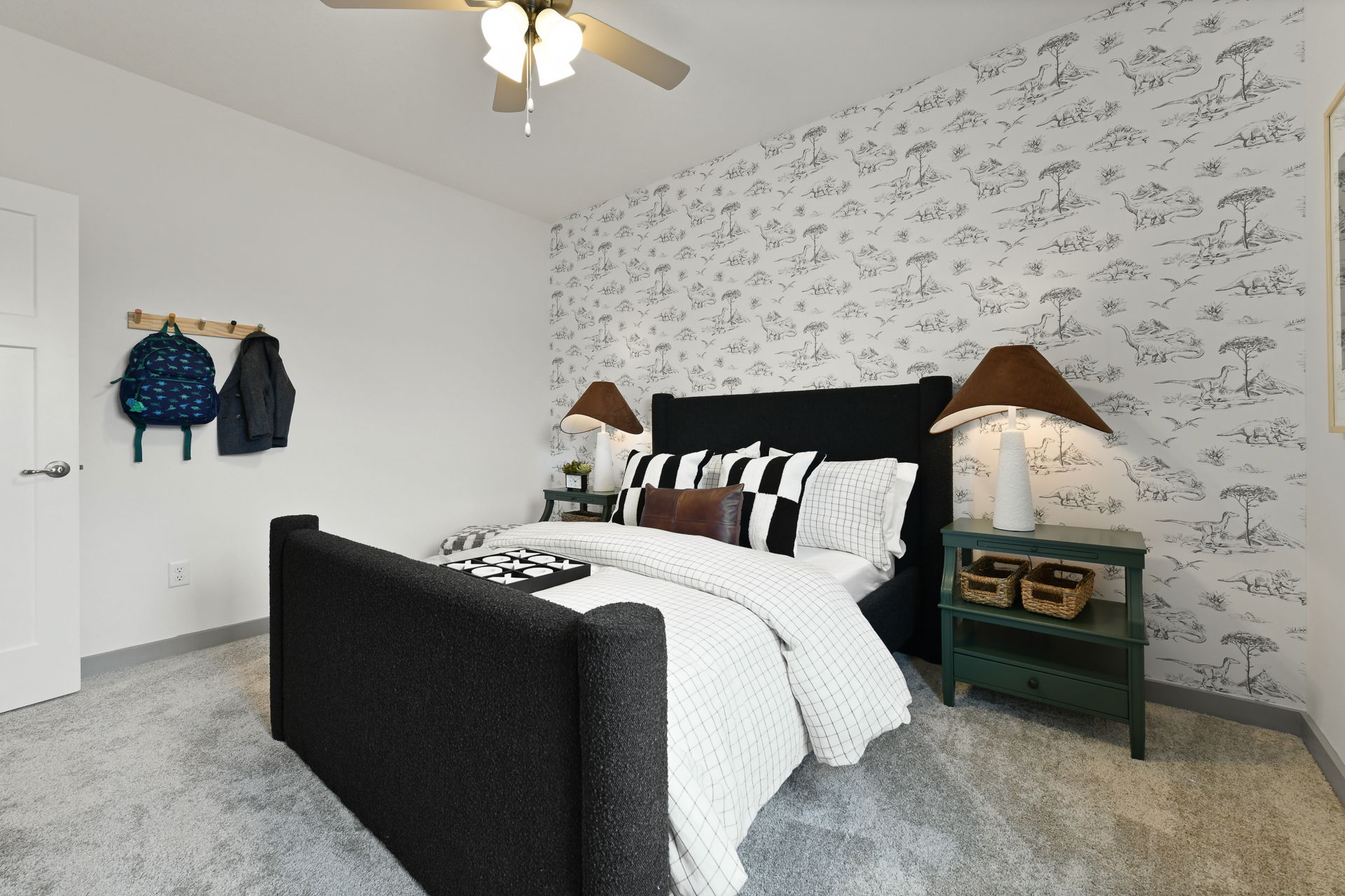 Stylish kid's bedroom featuring dinosaur-themed wallpaper, a black upholstered bed with checkered bedding, and cozy bedside lamps.