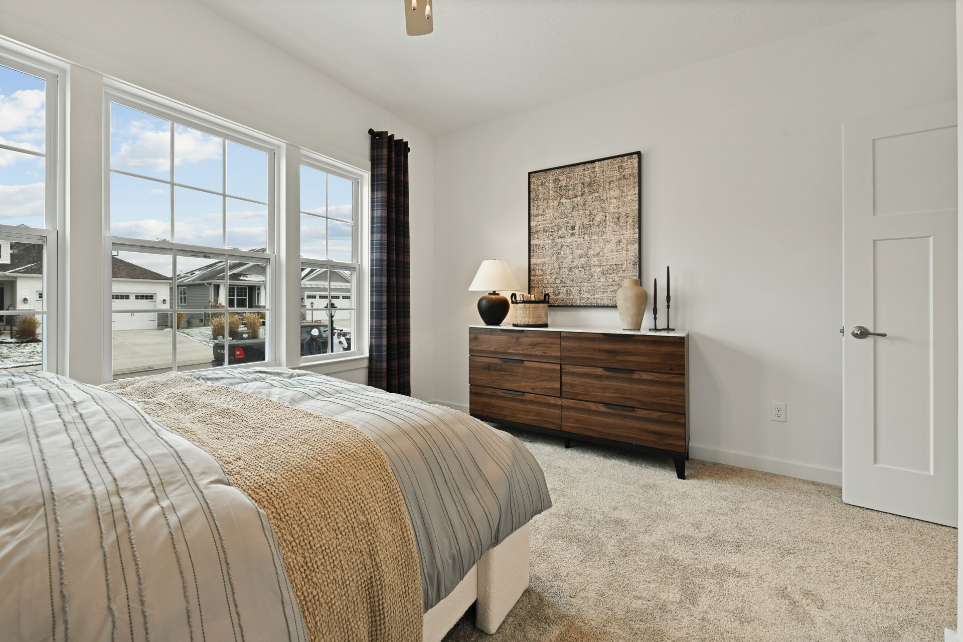 Modern bedroom interior with large windows, a comfortable bed, and a stylish wooden dresser.