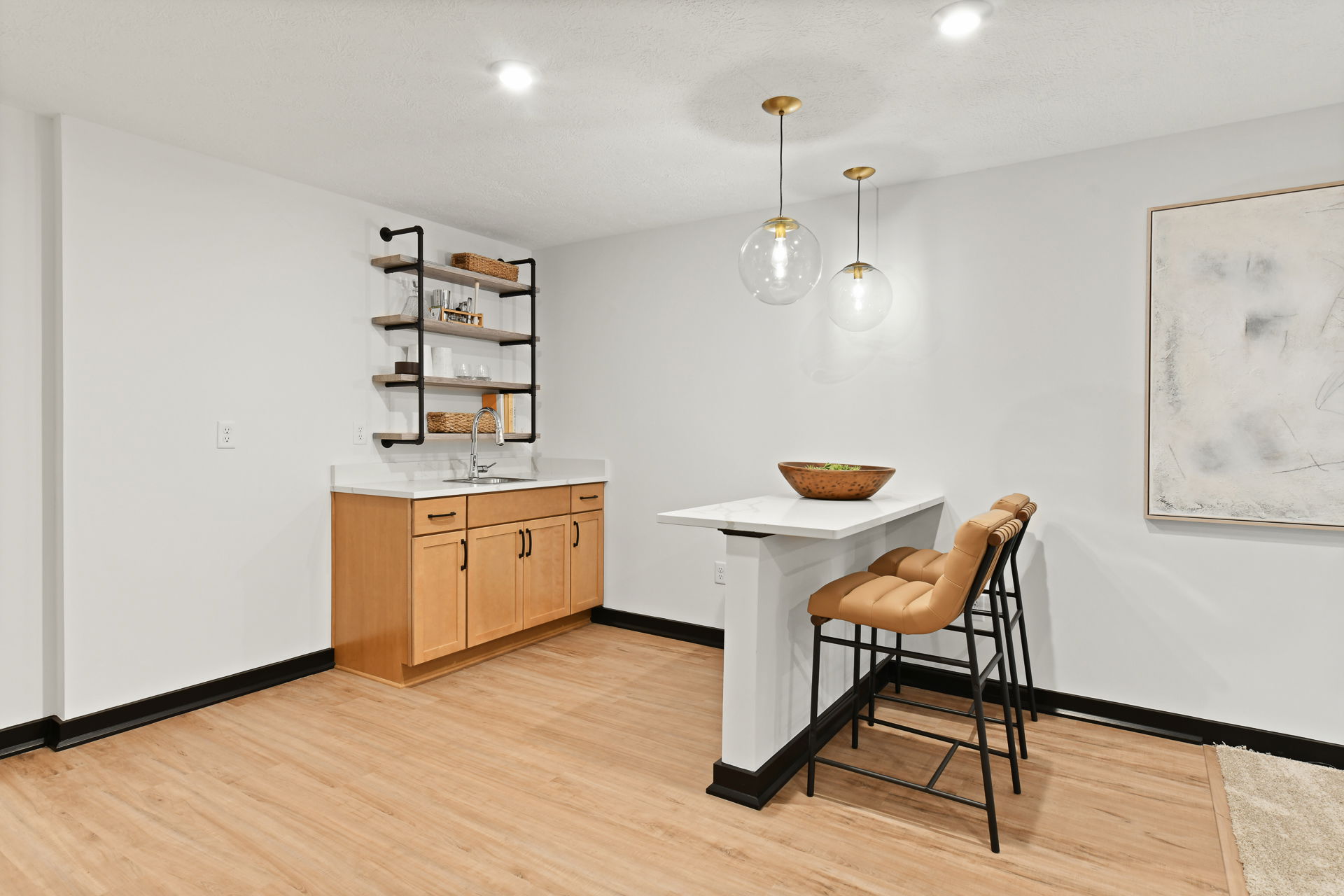 Modern basement bar with wooden cabinets, industrial shelves, pendant lighting, and a white marble counter with tan leather barstools.