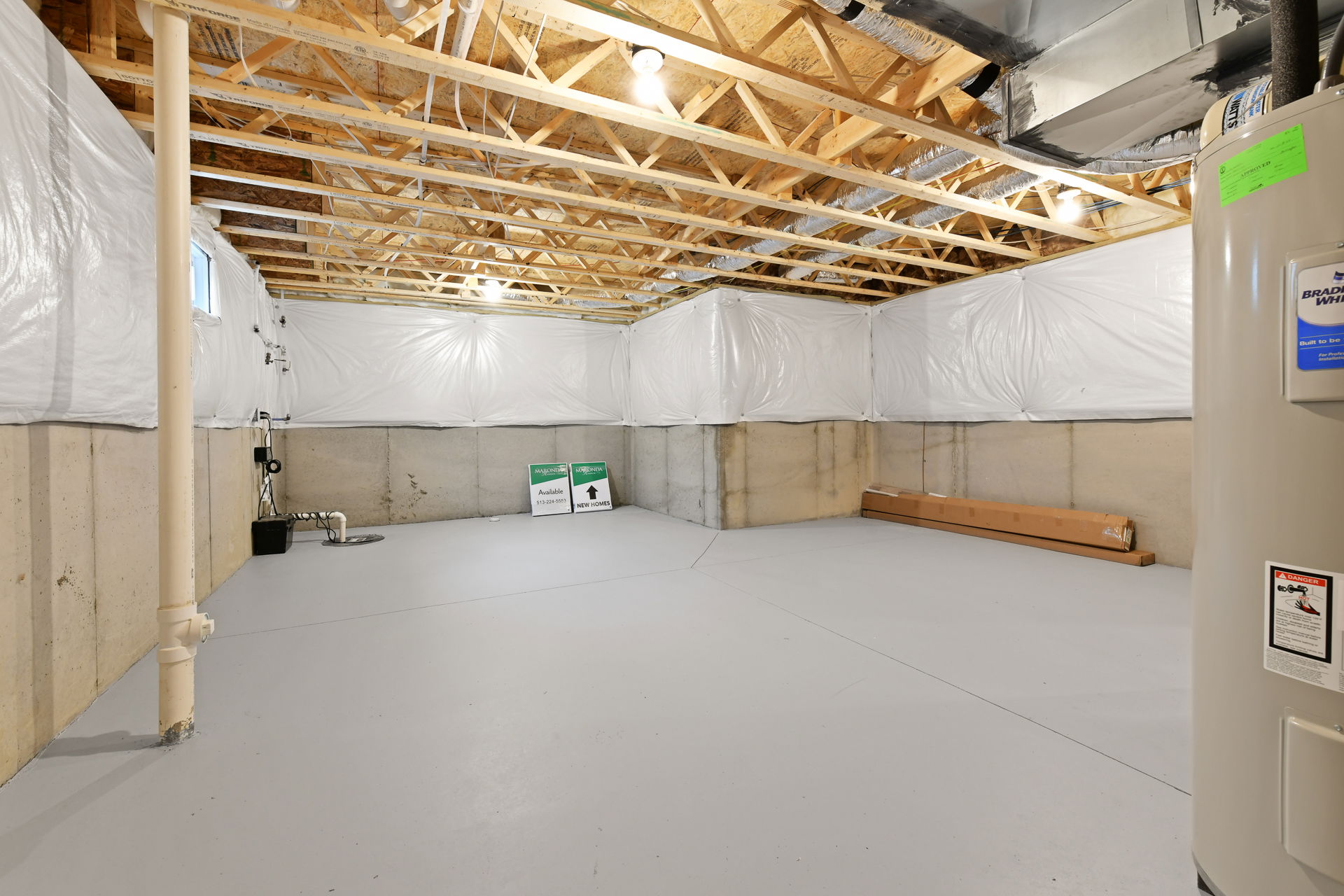 Unfinished basement with concrete floors, exposed wooden beams, and white insulated walls, ready for potential renovation.