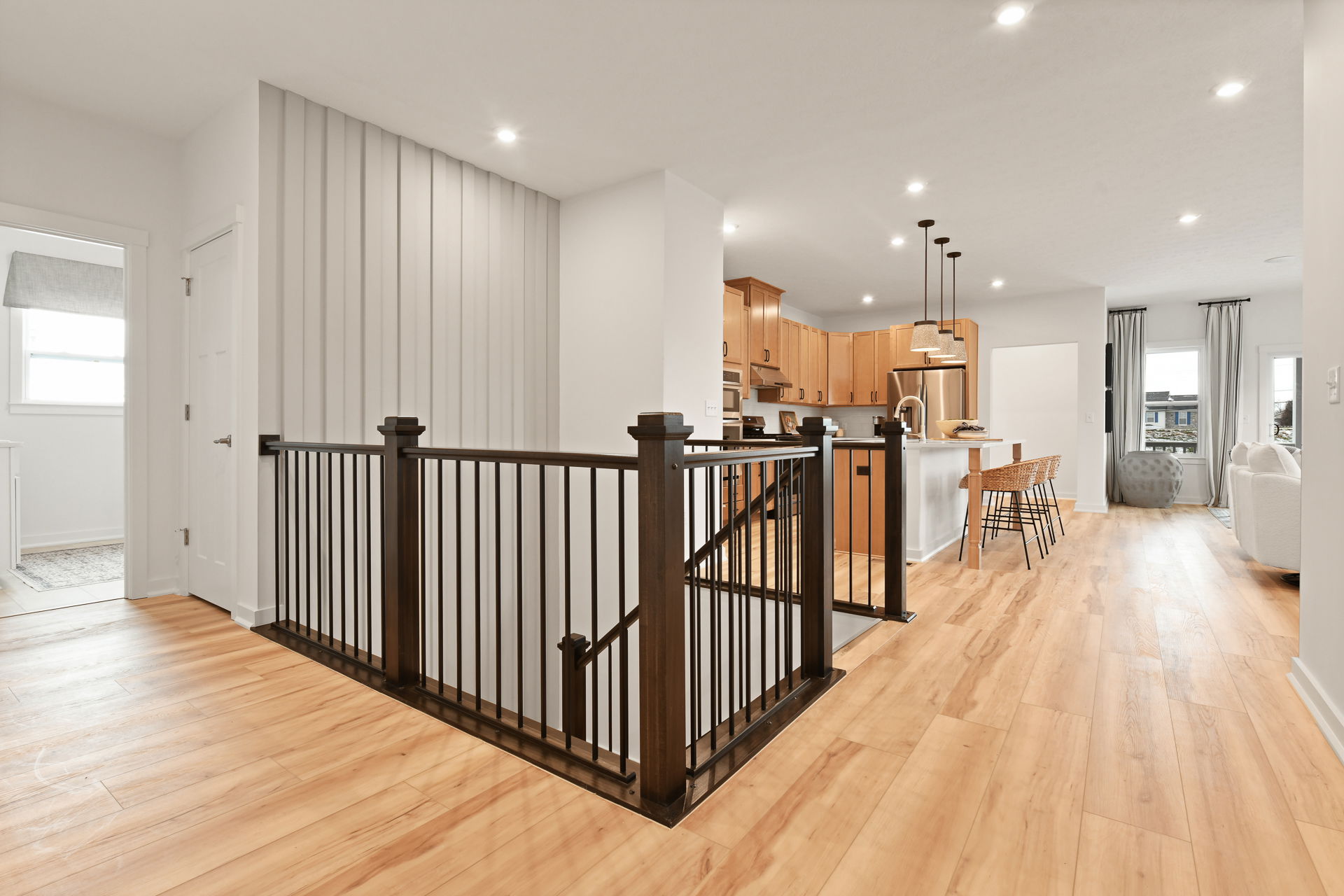 Modern open-concept kitchen and living area with wooden flooring, stylish lighting, and a black railing staircase.