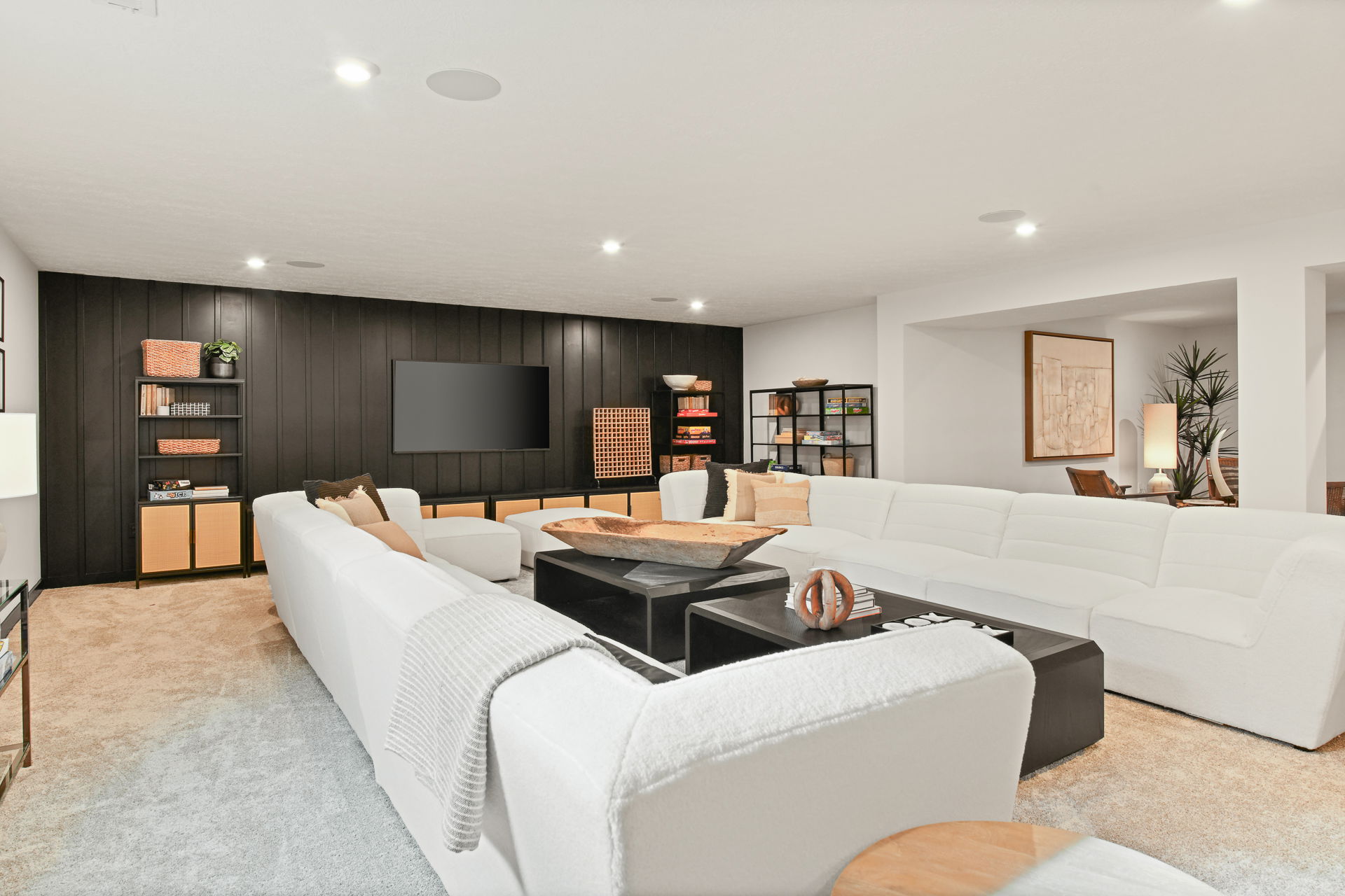 Modern living room with white sectional sofas, black accent wall, and stylish shelving.