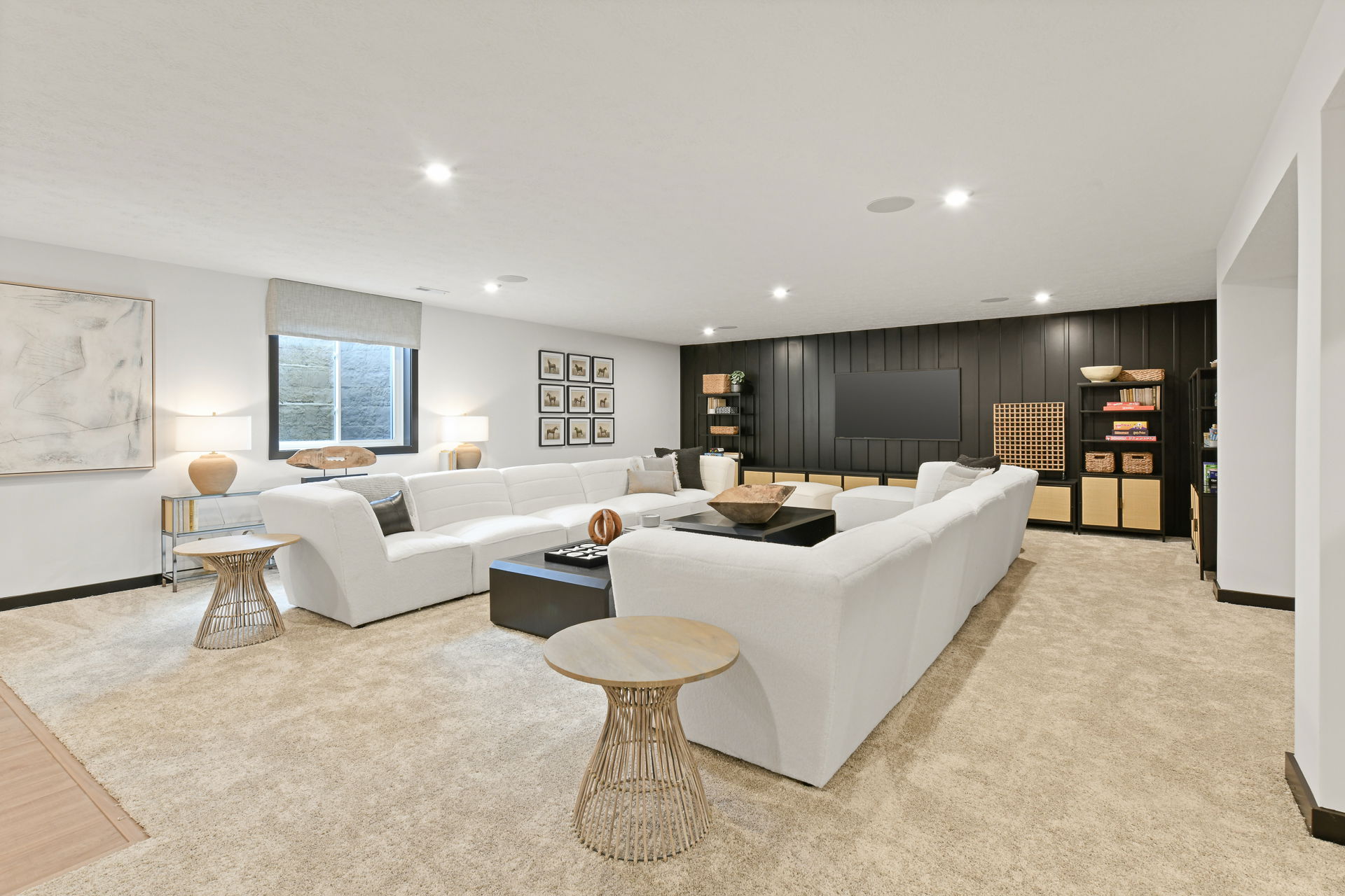 A modern basement entertainment room with a large white sectional sofa, wall-mounted TV, and stylish decor.