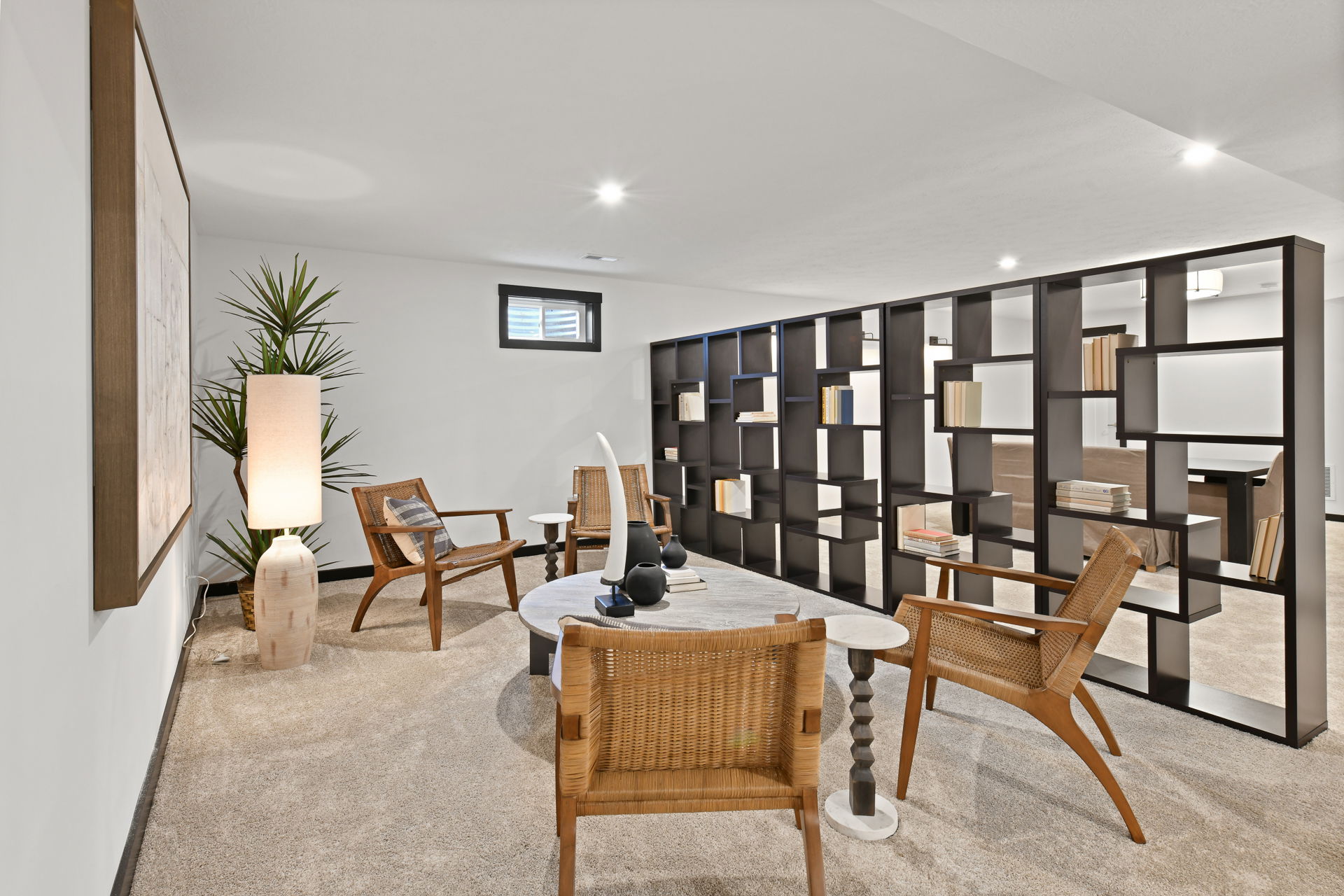 Modern home office with wicker chairs, bookshelves, and stylish decor in a well-lit room.