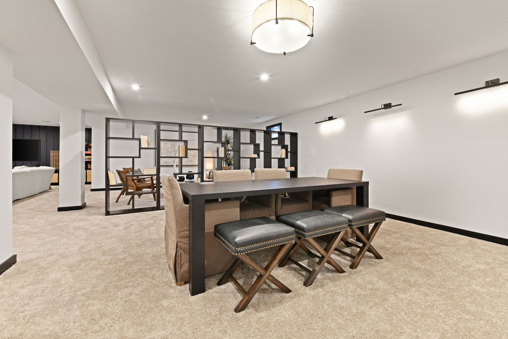 Modern basement interior with a black dining table, beige chairs, and a stylish room divider.