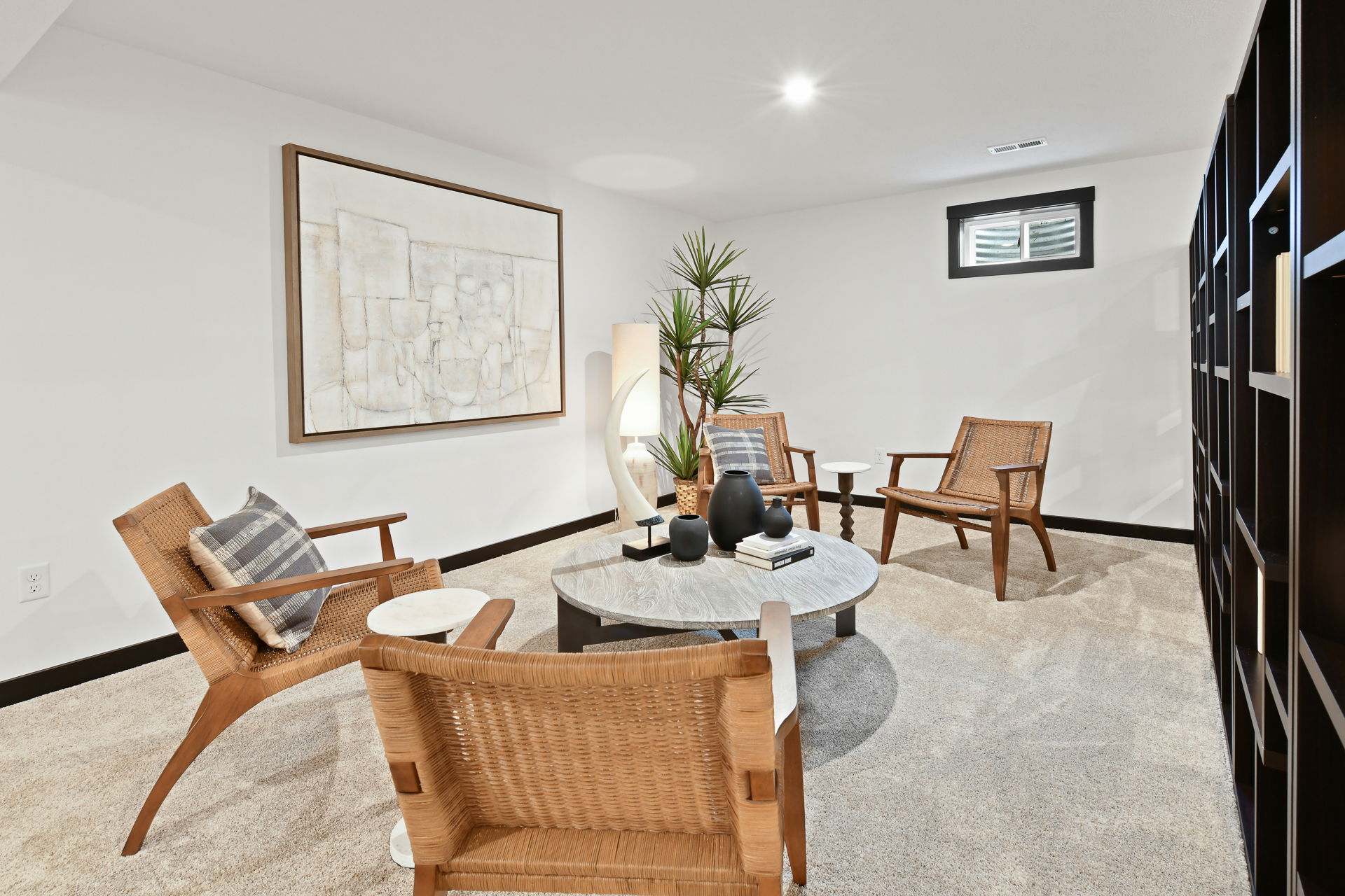 Modern basement living room with wicker chairs, a round coffee table, decorative items, and abstract wall art.