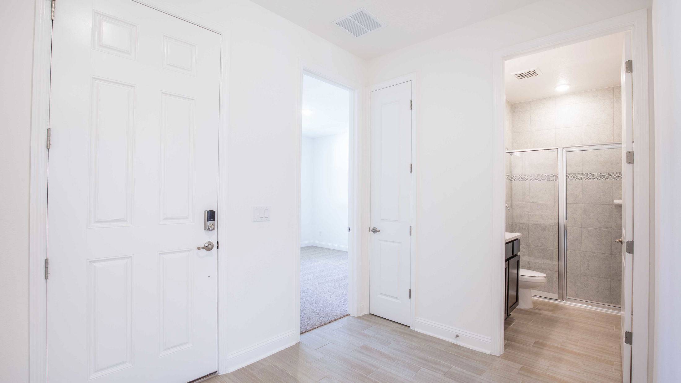Bright, modern interior featuring white walls, a wooden floor, an open bedroom door, and an adjacent tiled bathroom with a shower.