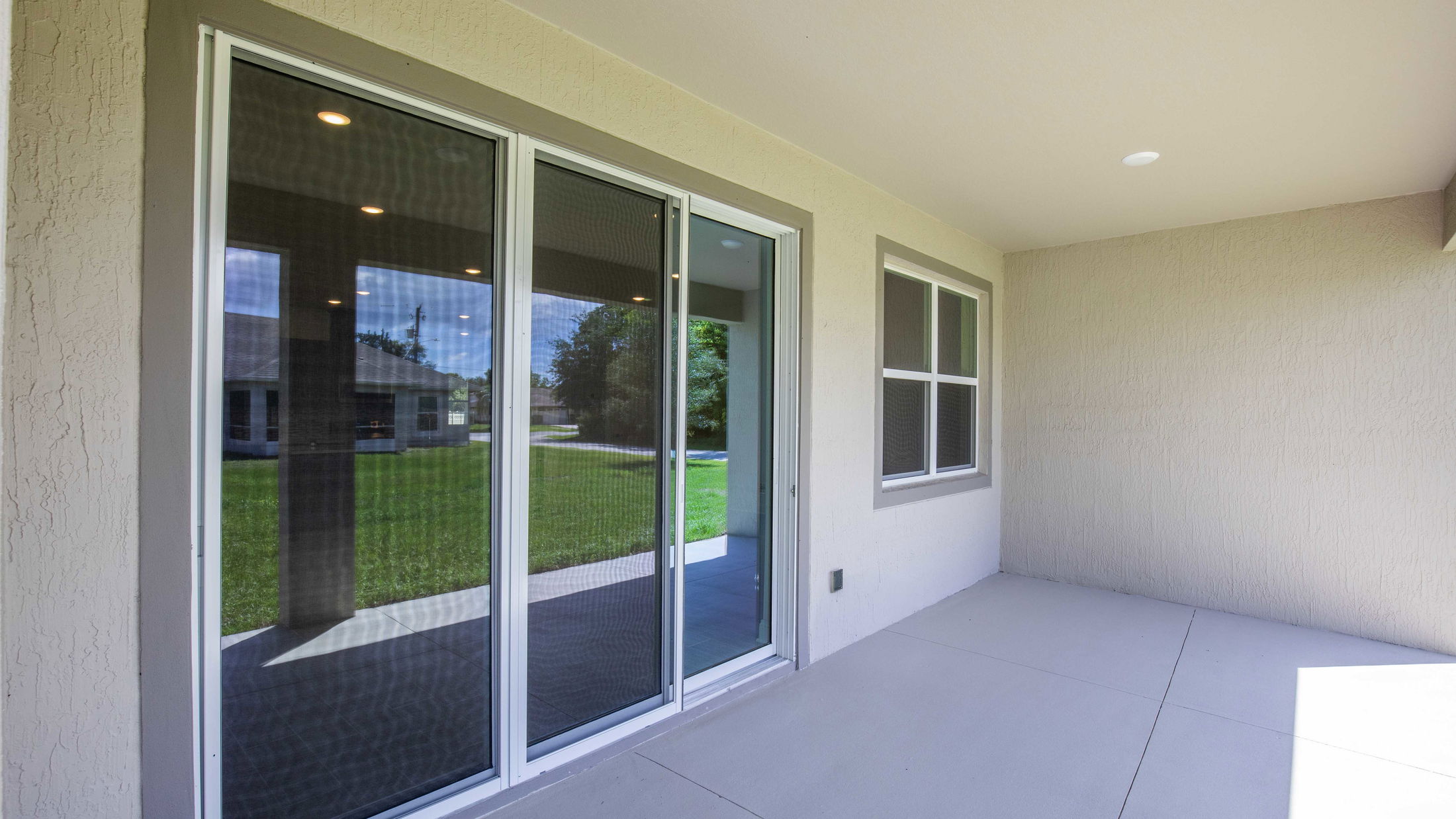 Covered patio area with sliding glass doors and a view of a green lawn and neighboring house.