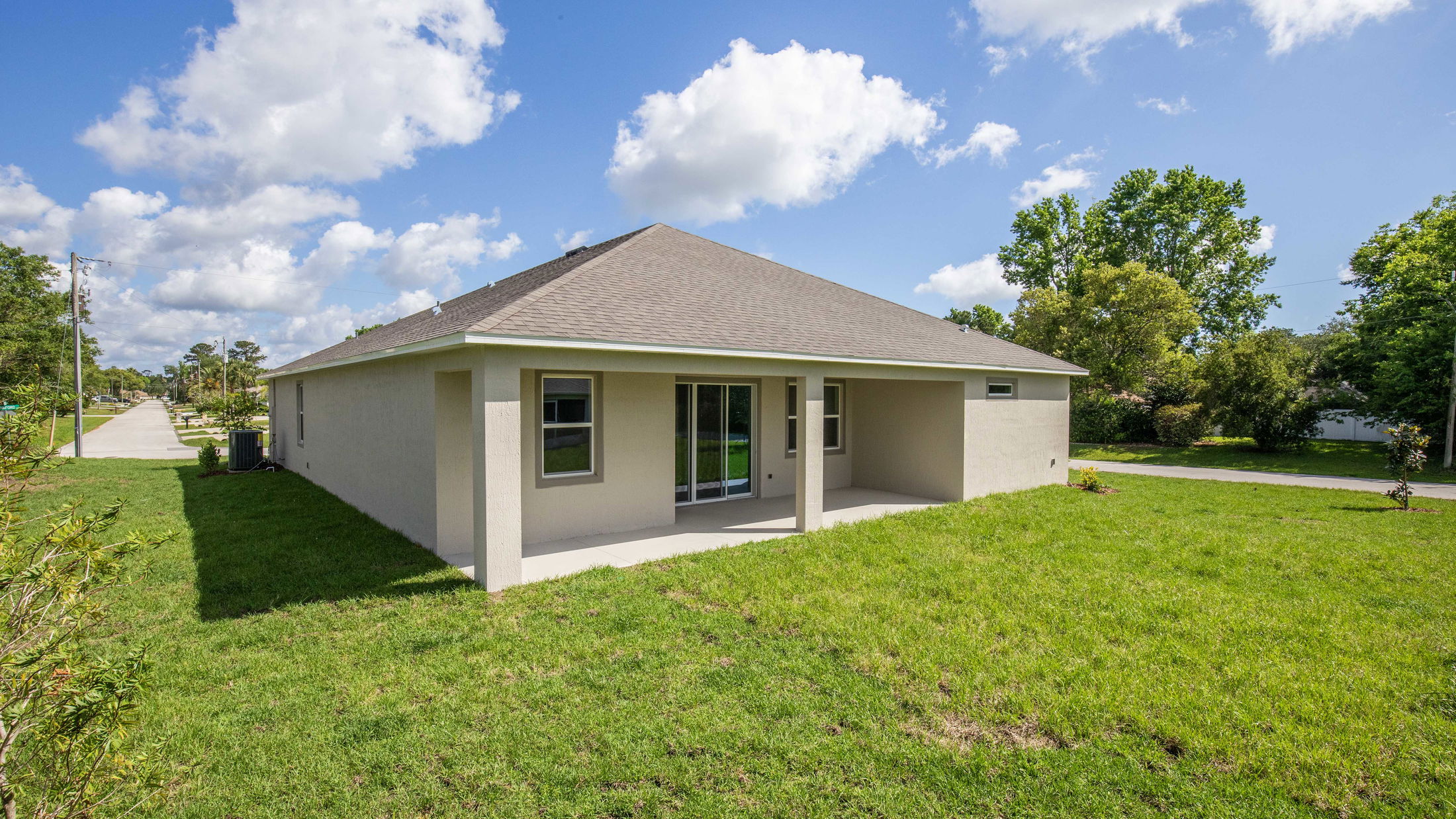 New beige single-story house with a covered patio, set on a lush green lawn under a clear blue sky.
