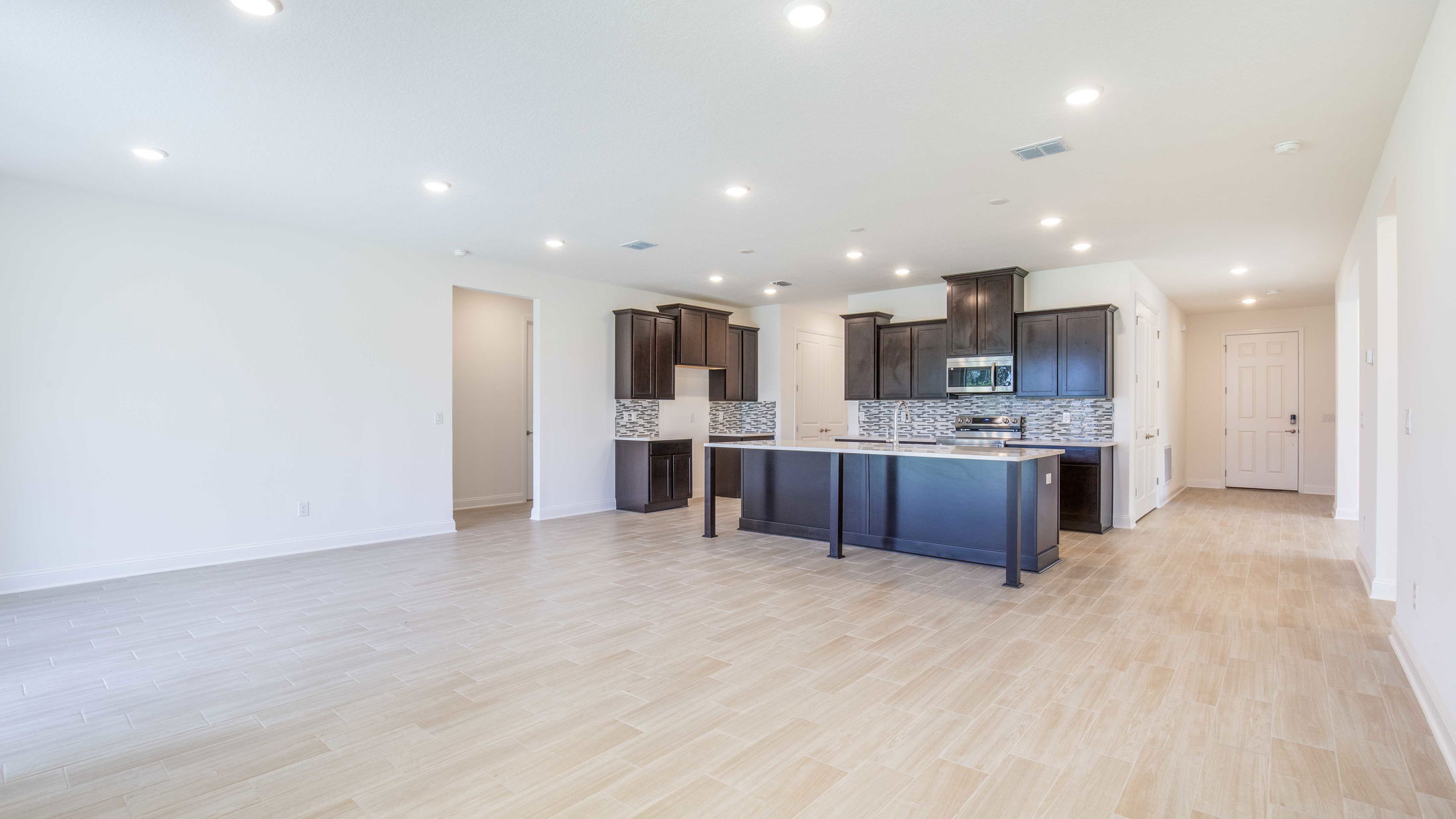Spacious modern kitchen with dark wooden cabinets, tile flooring, and recessed lighting in an open-concept layout.