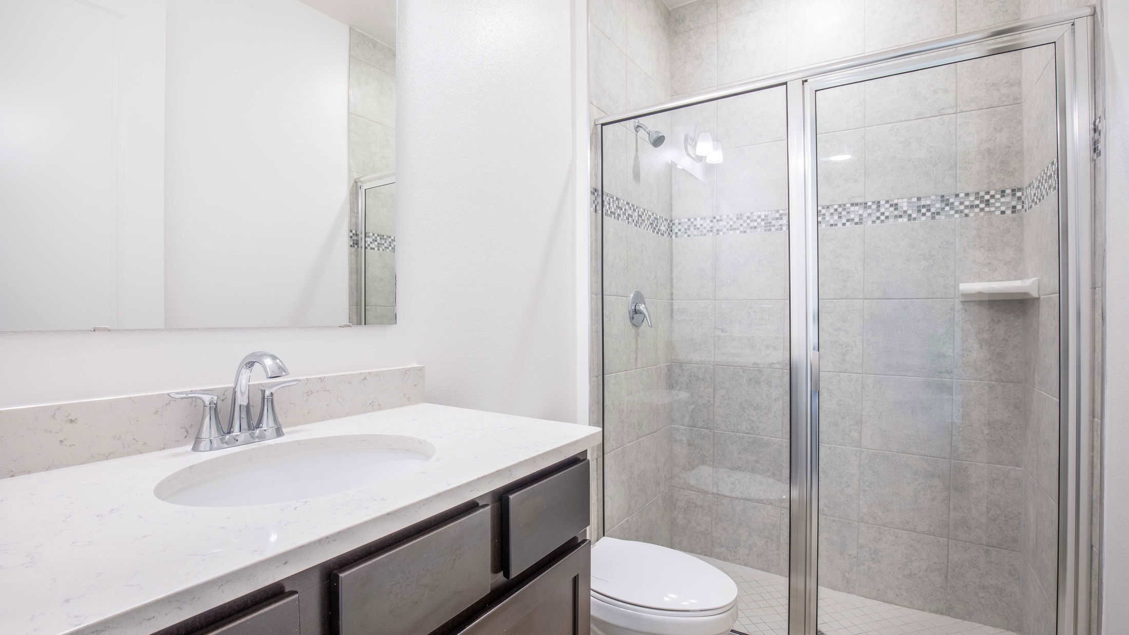 Modern bathroom interior featuring a sleek white countertop, undermount sink, and a glass-enclosed shower.