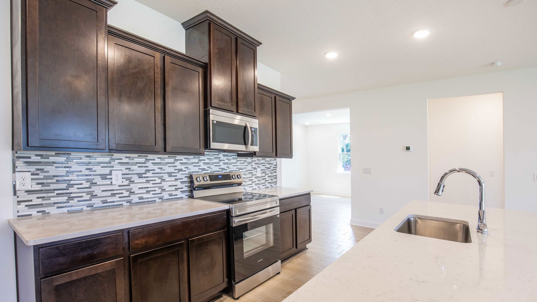 Modern kitchen interior with dark wood cabinets, stainless steel appliances, and a white marble countertop.