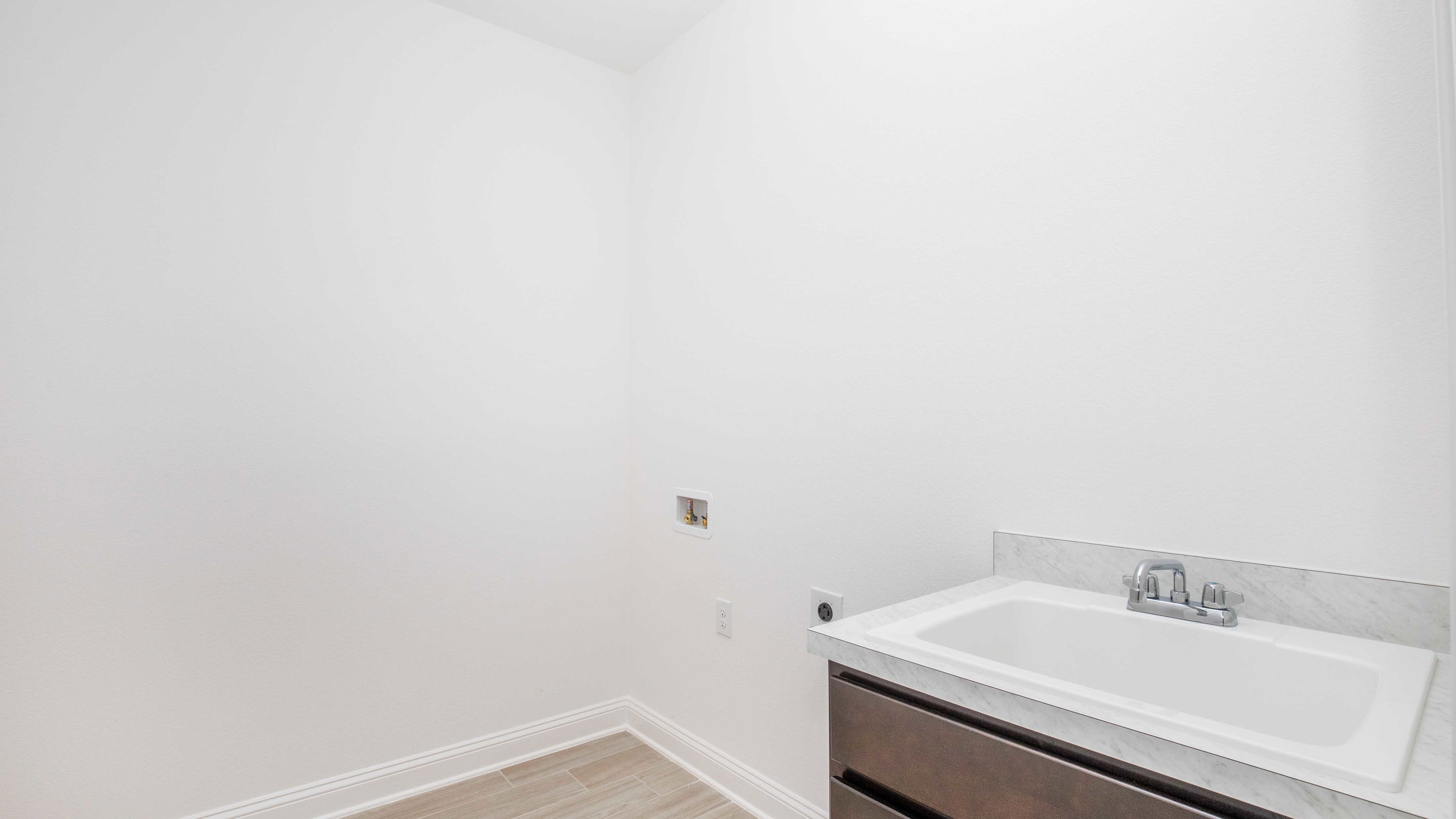Modern laundry room interior with a white utility sink and marble countertop against a minimalistic white wall.