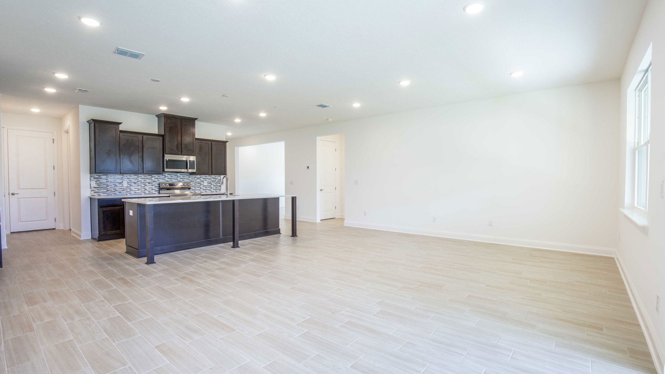 Modern open-plan kitchen and living area with wooden flooring, light walls, dark wood cabinets, and a central island.