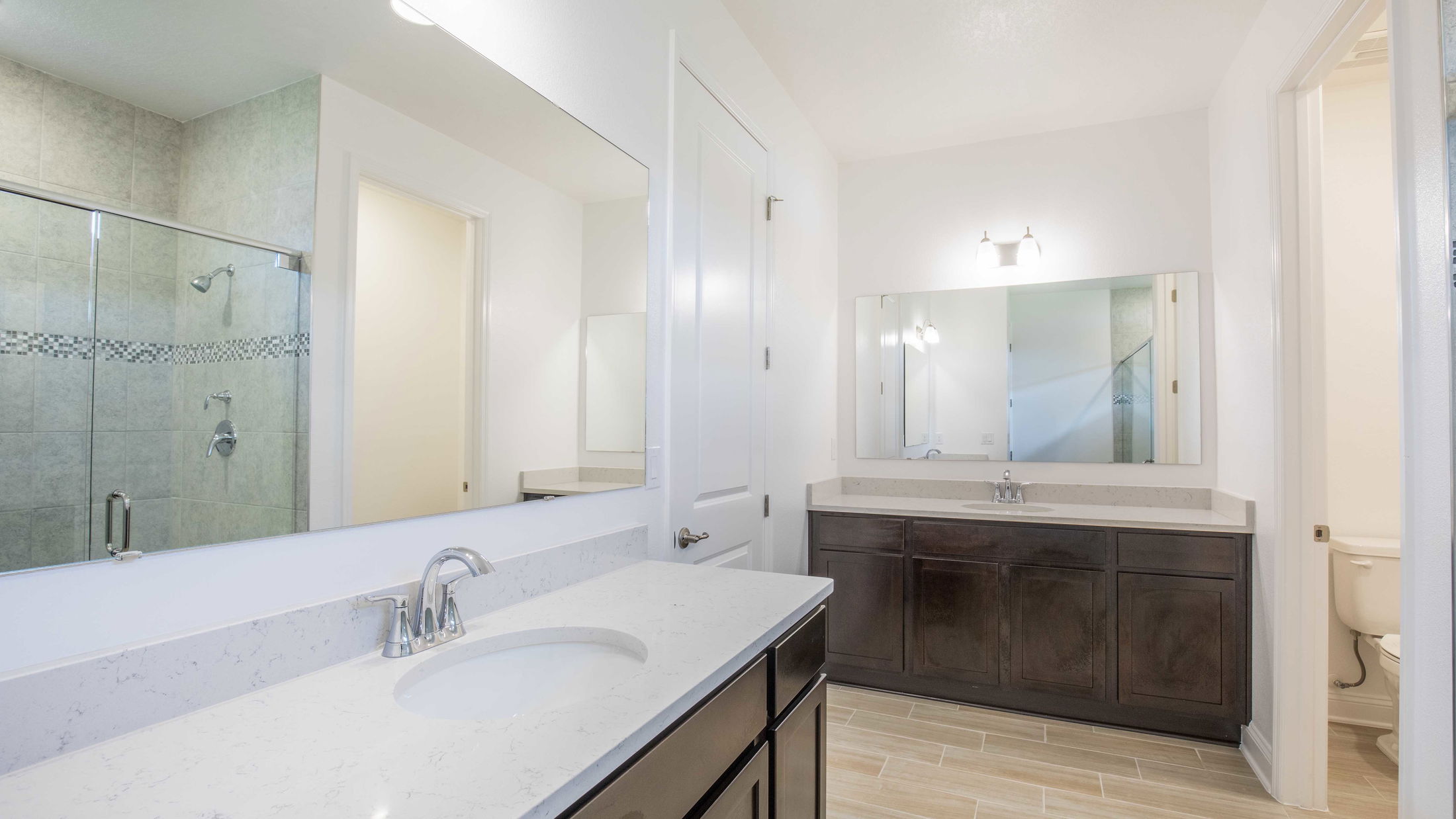 Modern bathroom with dual sinks, marble countertops, a glass shower enclosure, and wood cabinetry.