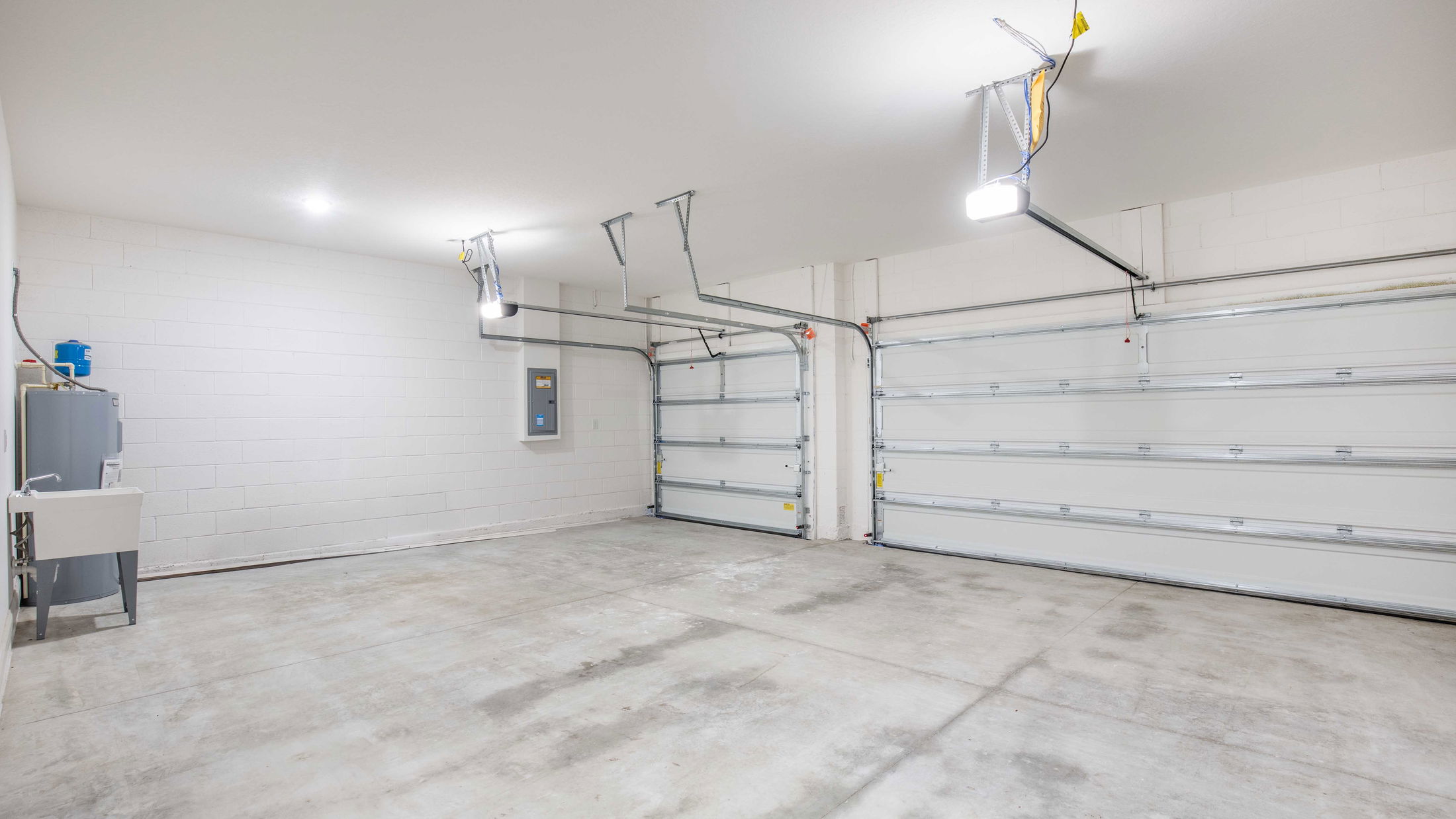 Spacious, well-lit garage interior with double doors, featuring a utility sink and water heater.